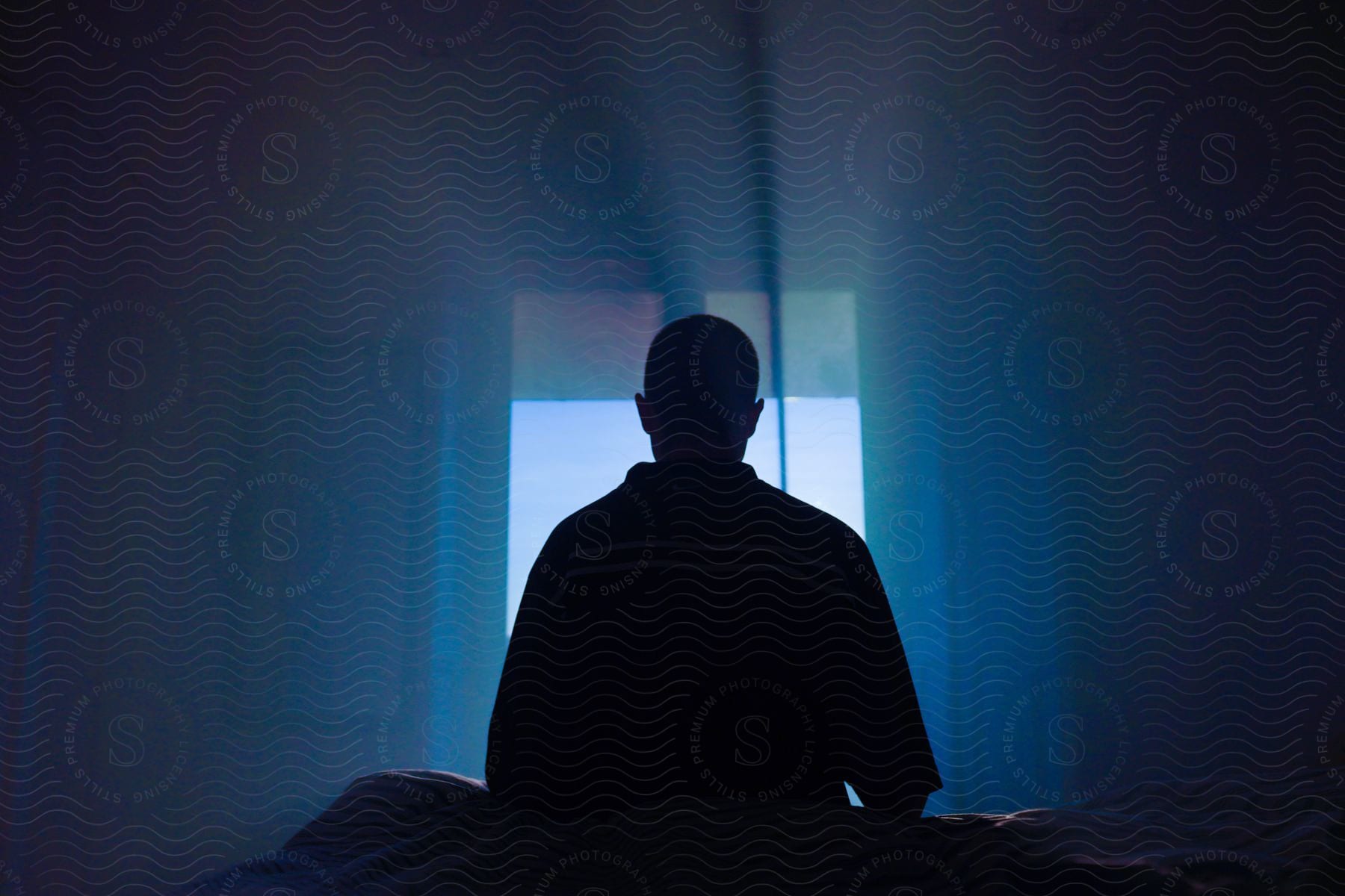 A man sitting on the floor in a dark room blocking light from the window