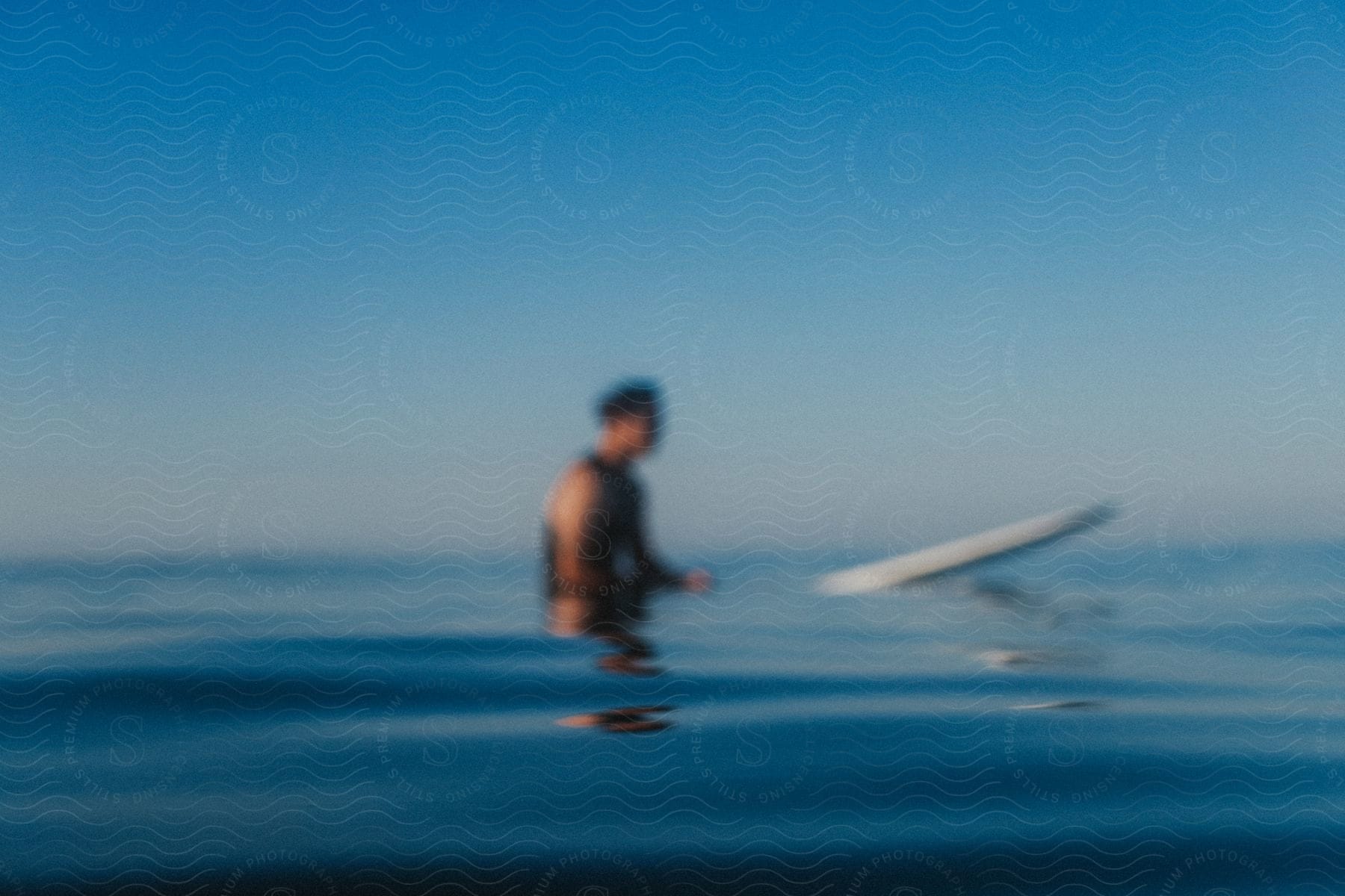 A man sits on a surfboard in reflective blue water on a clear day