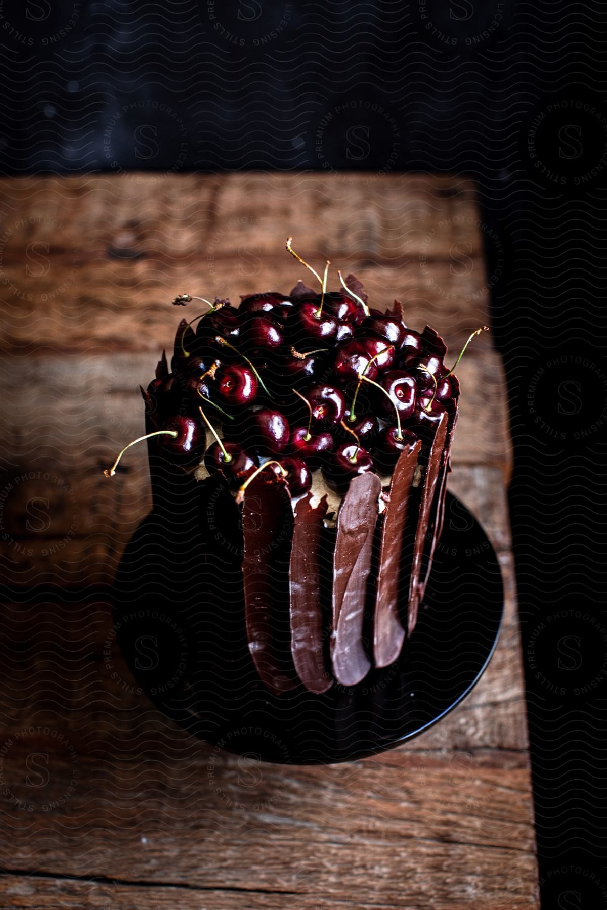 A small chocolate cake with cherries on top placed on a black plate on a wooden table