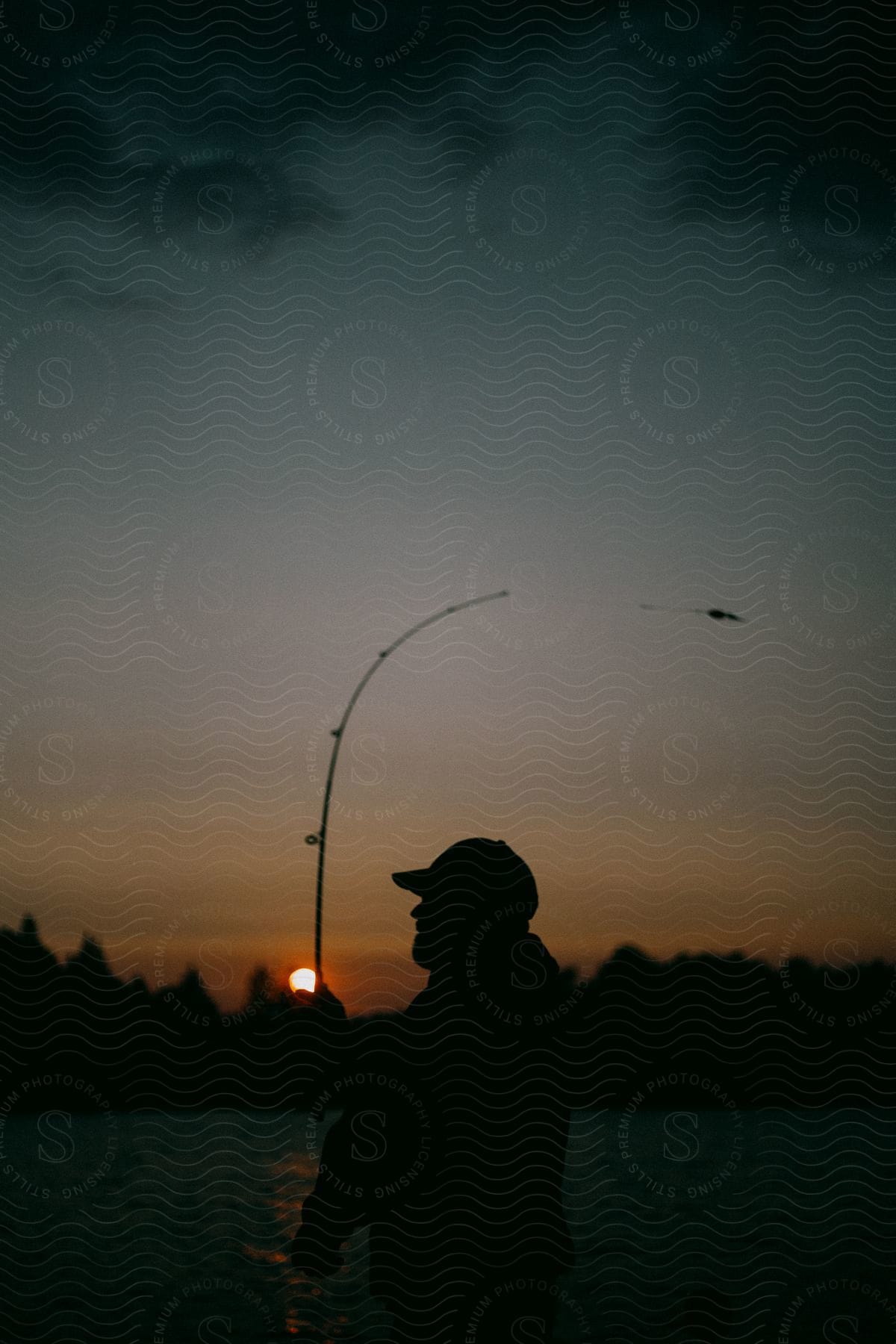 A man wearing a ball cap is standing in a body of water and flyfishing at sunset