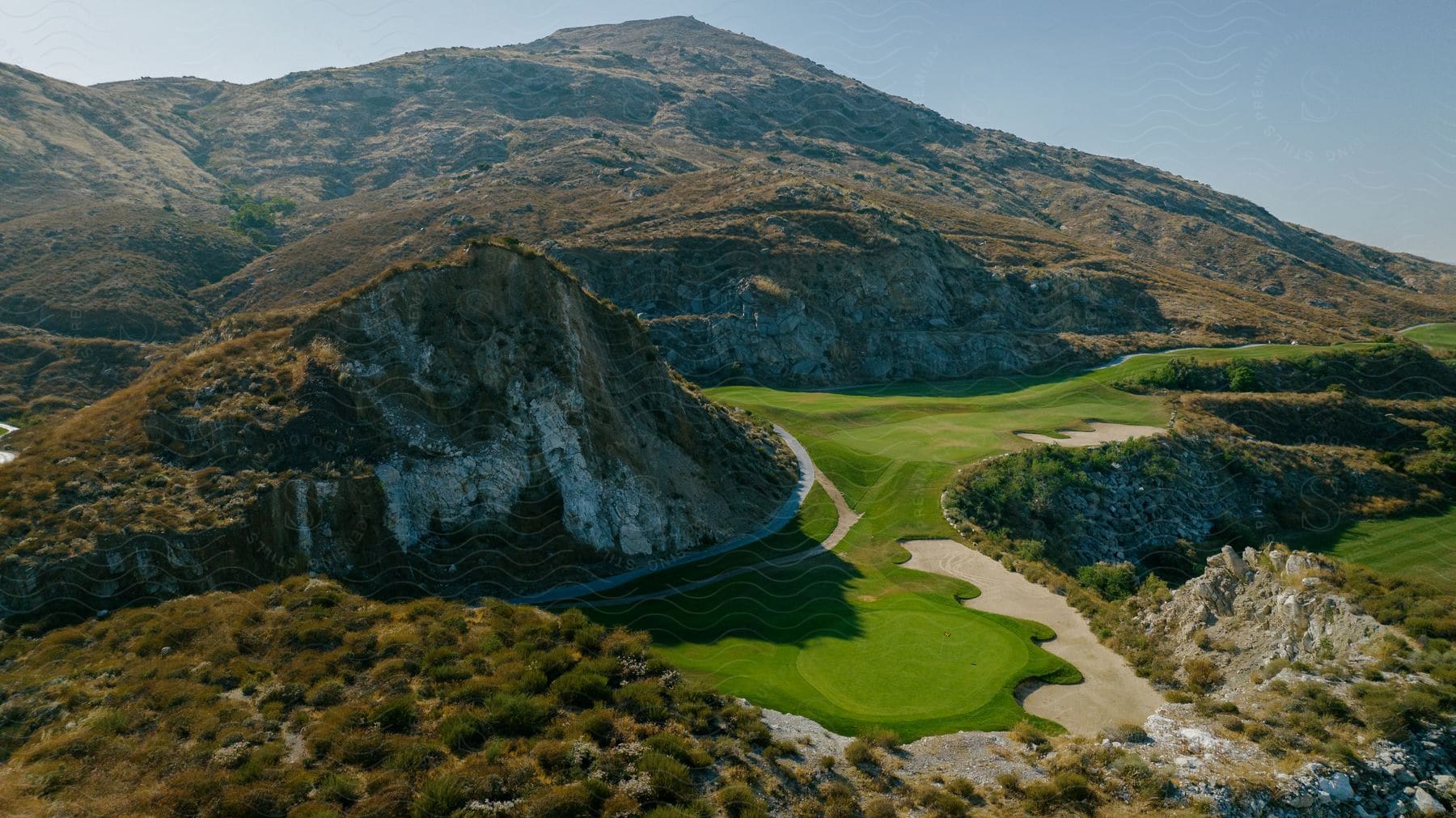 An aerial view of a golf course located at the base of a mountain range on a sunny day