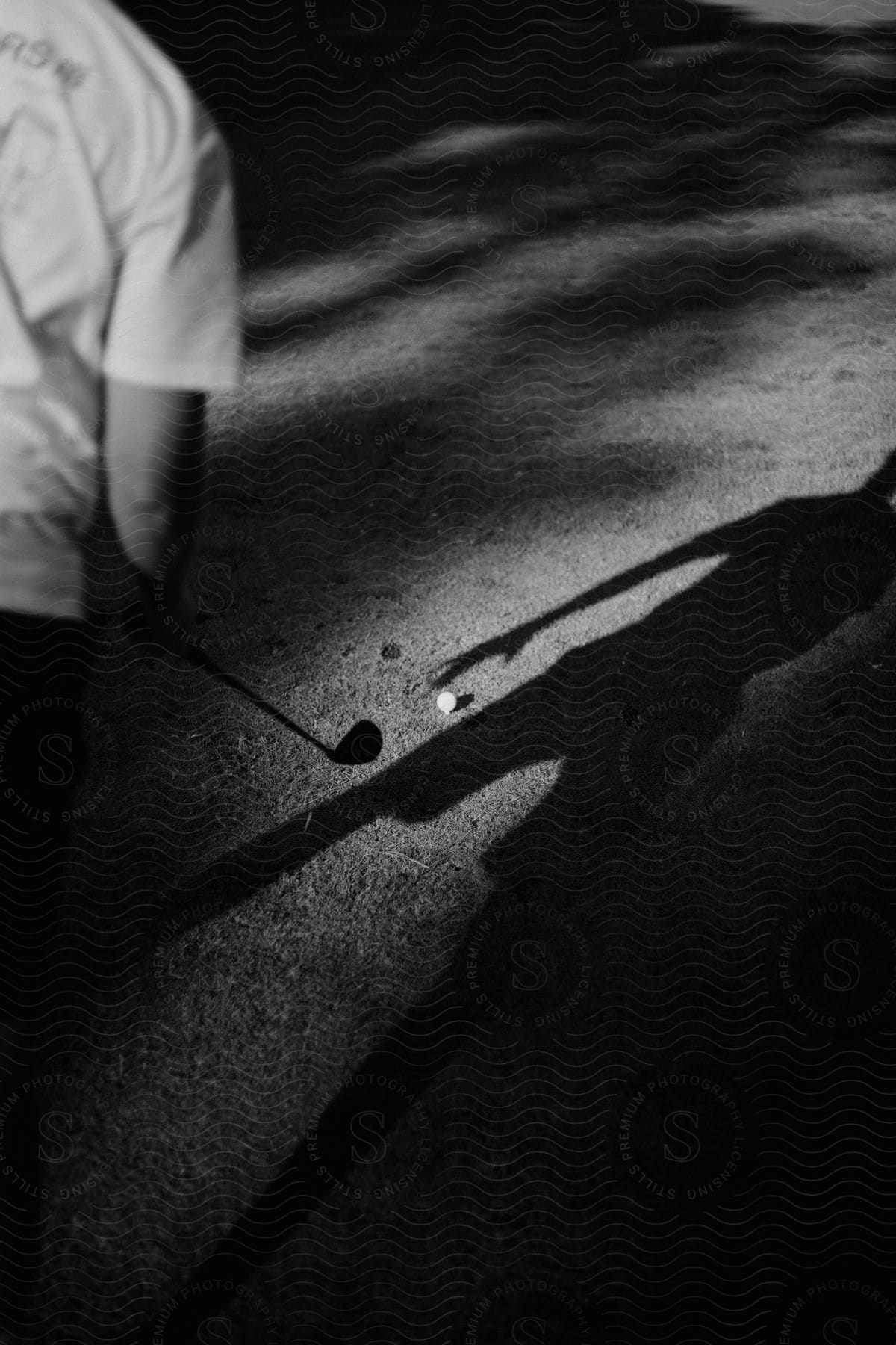 A man holding a golf club with his body silhouette visible in his shadow