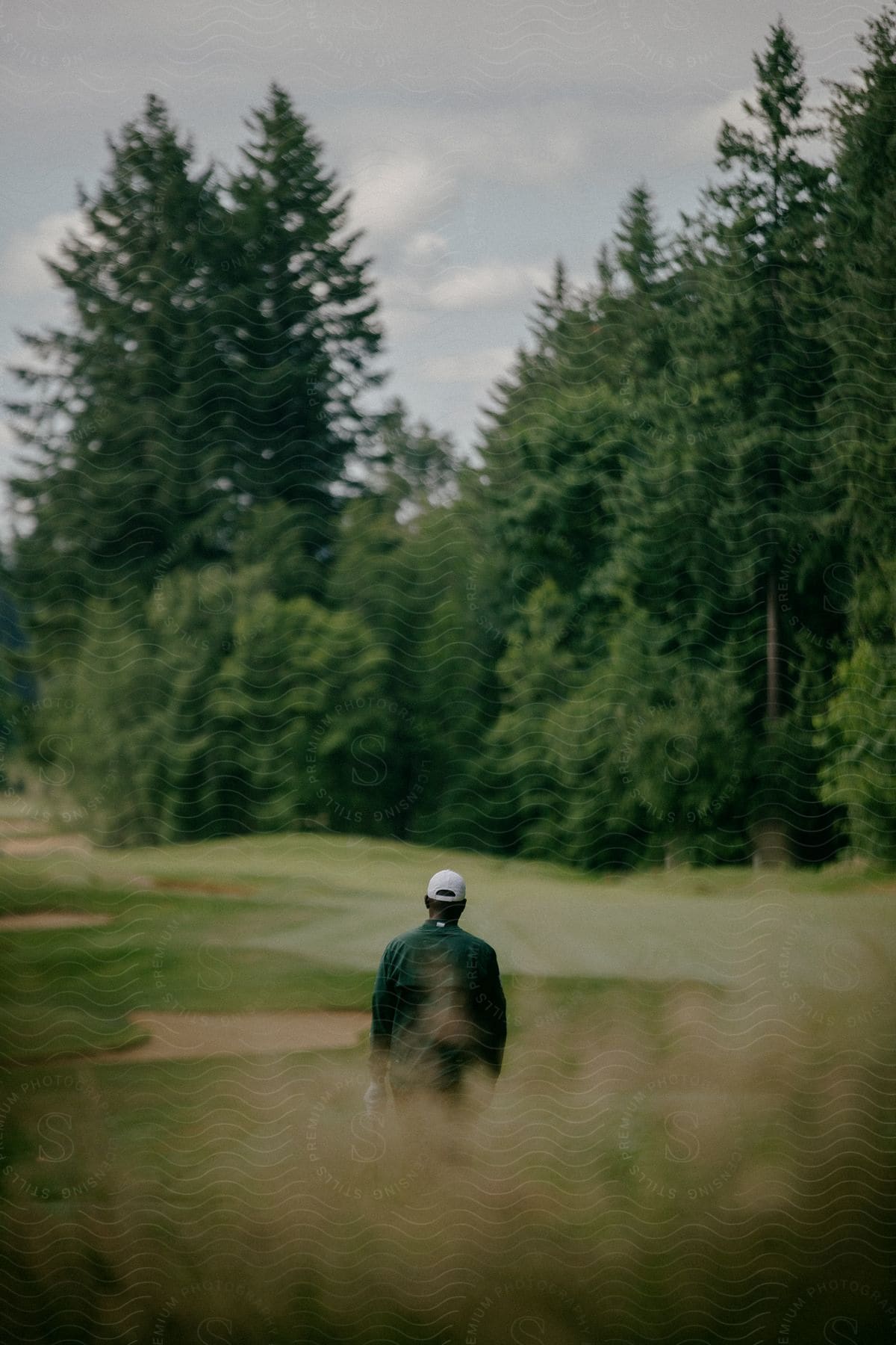 A man walking towards a green playing field on a golf course