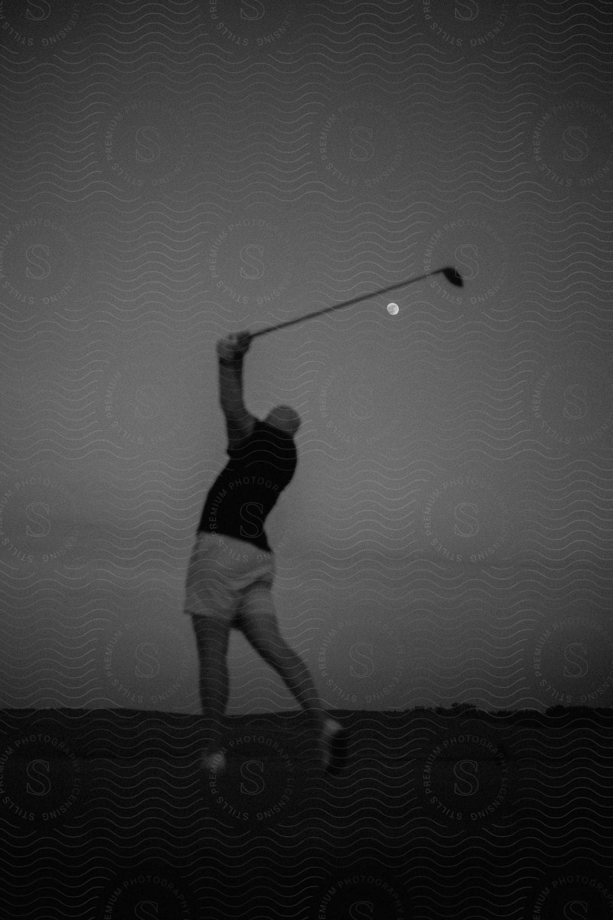 A golfer swings their golf club high in the air as the moon glows in the sky