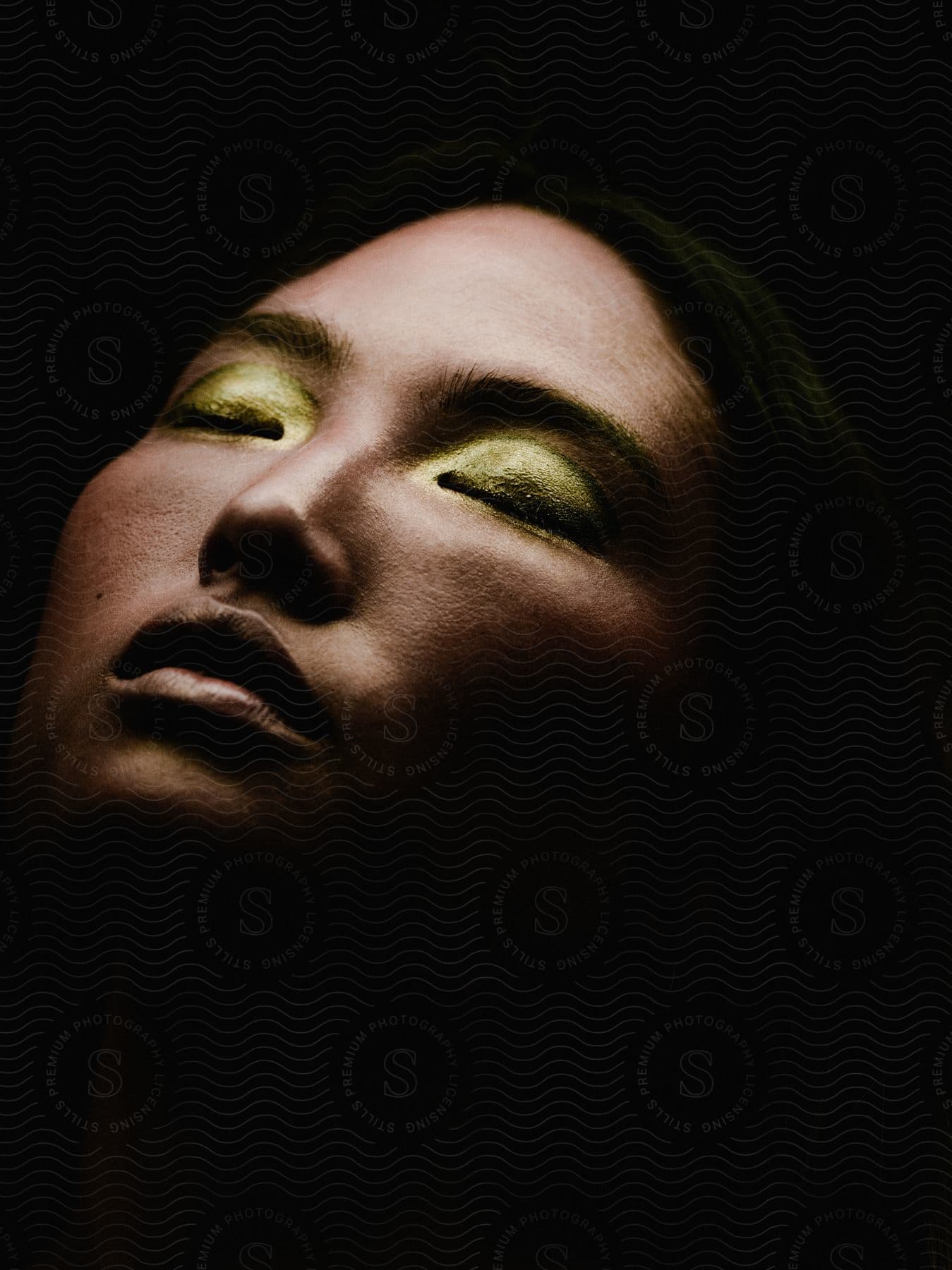 Stock photo of the face of a woman, eyes closed, wearing gold eye shadow.