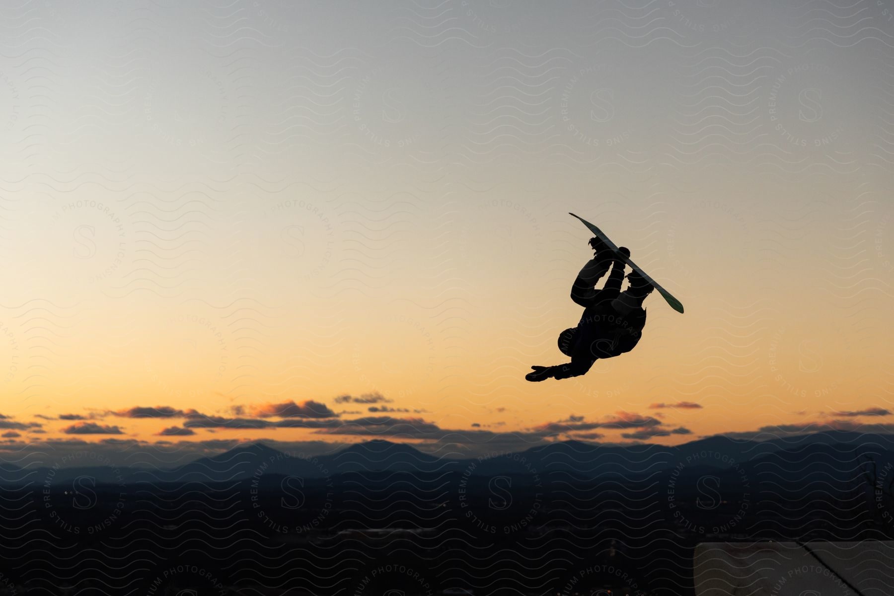 In the evening, a dark, dramatic shadow is cast as a man performs a daring stunt mid-air on a snowboard.