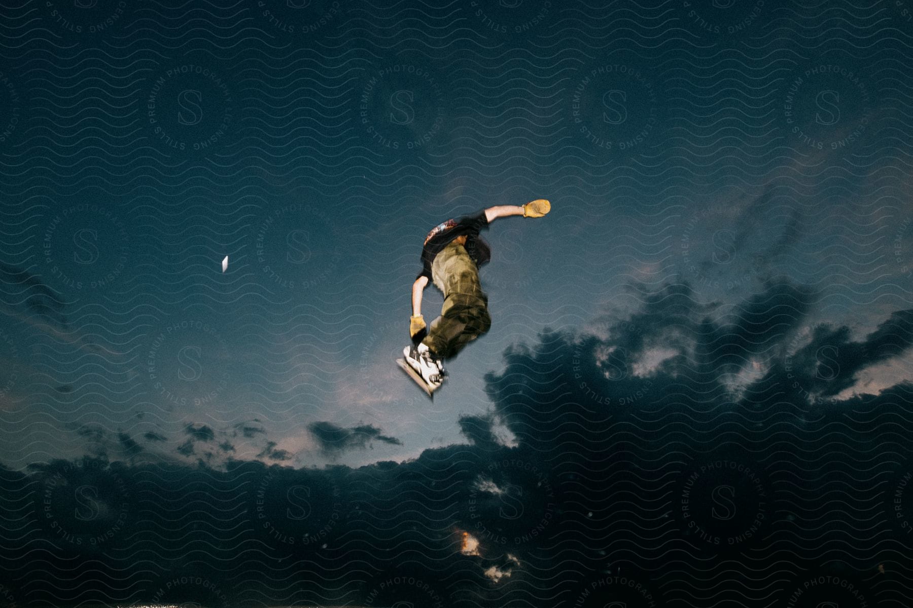 A person performing a skateboarding trick in the air against a dark dusk sky.