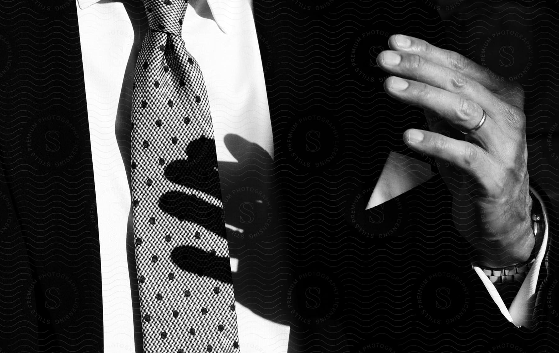 Man's hand casts shadow onto man's spotted tie.