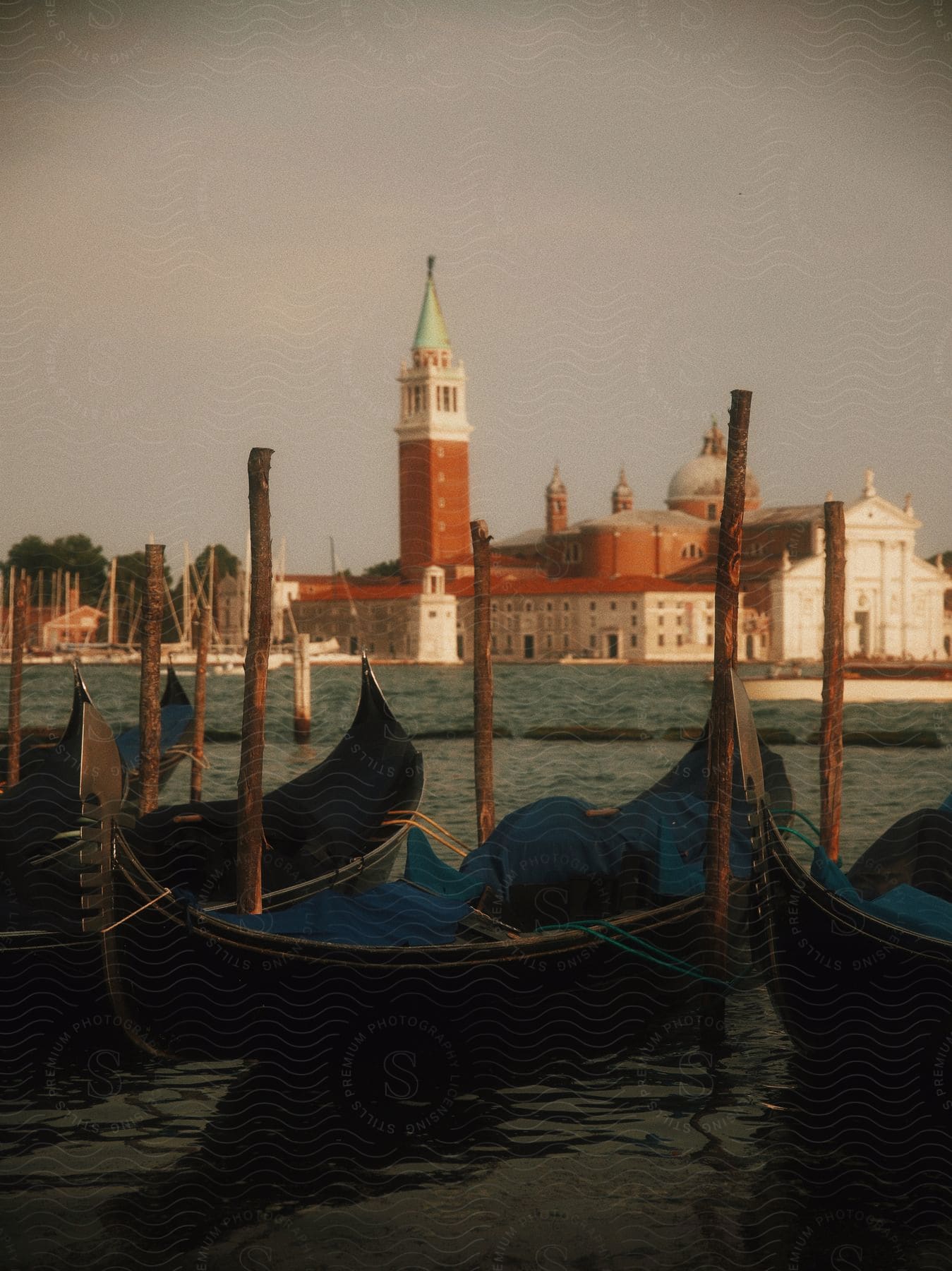 Gondolas float on the water with buildings and a tower along the coast