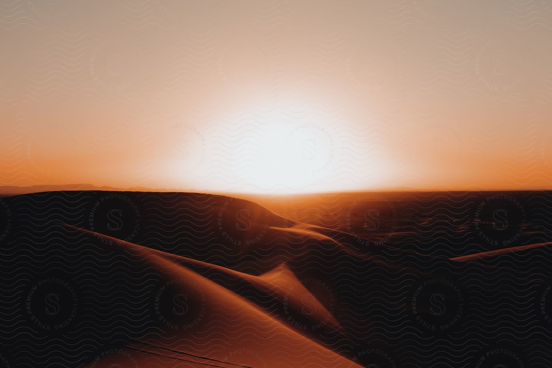 A lone sand dune silhouetted against a fiery sunset in the desert.