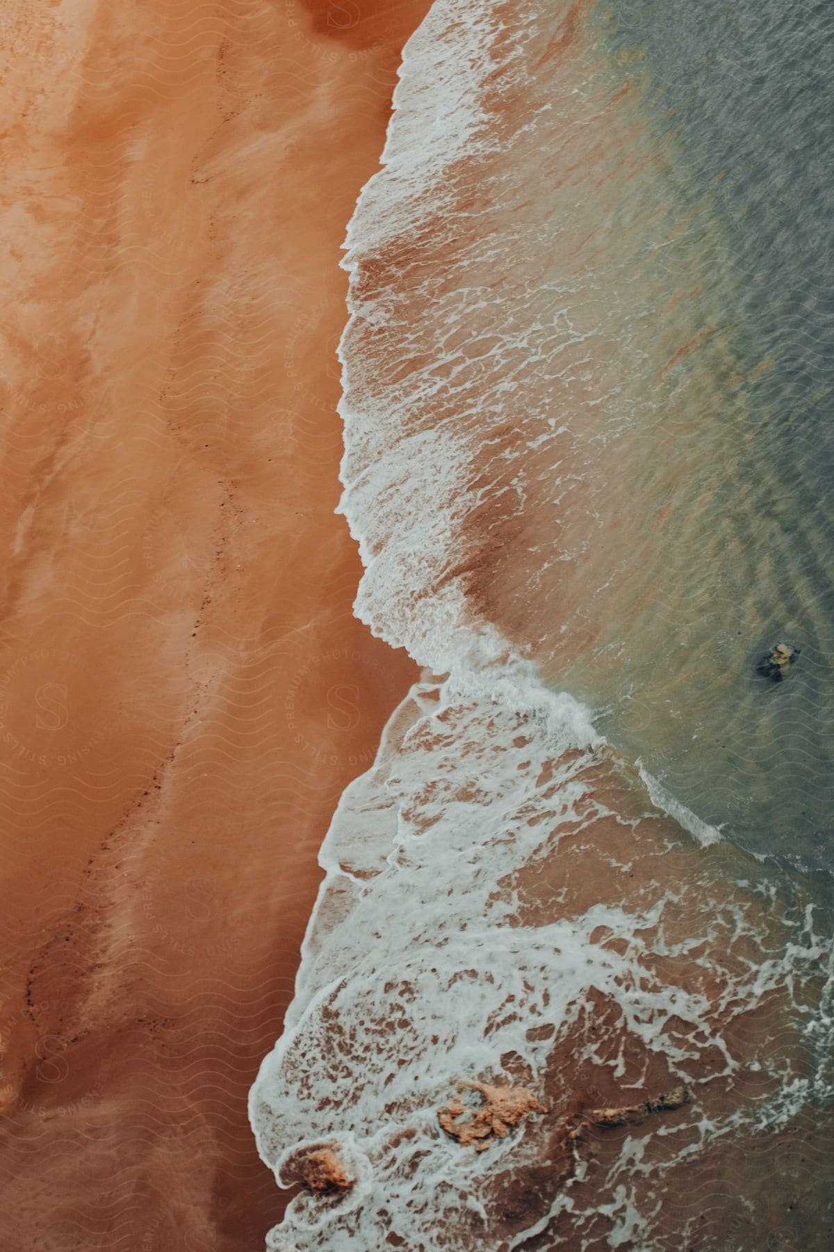 Stock photo of blue green surf foams as it flows on to red beach.