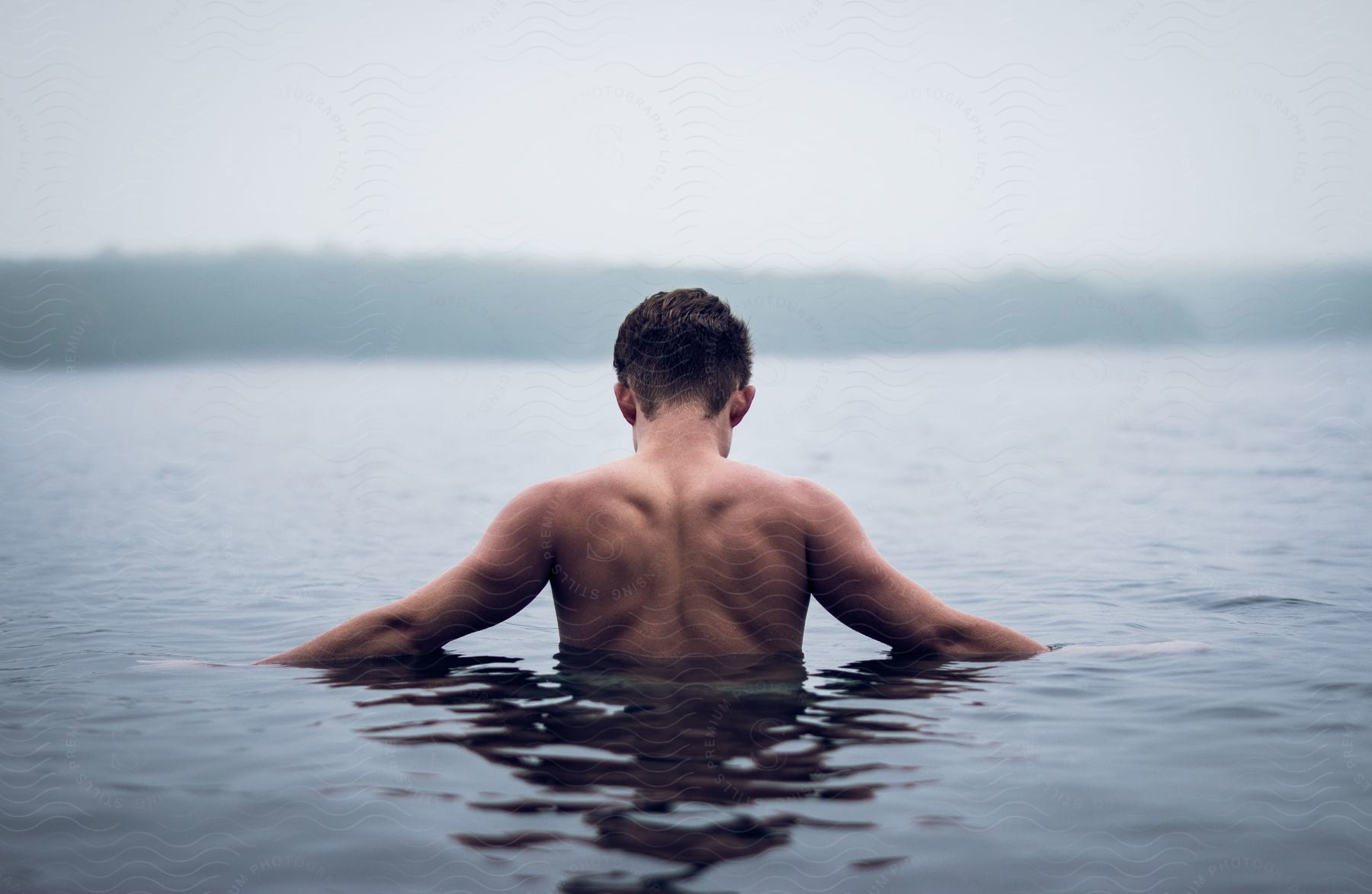 male person from the back standing with half their body covered in water close to a coast