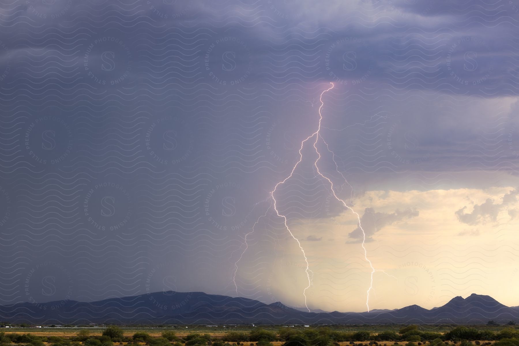 Lightning strikes misty mountains near town during storm.