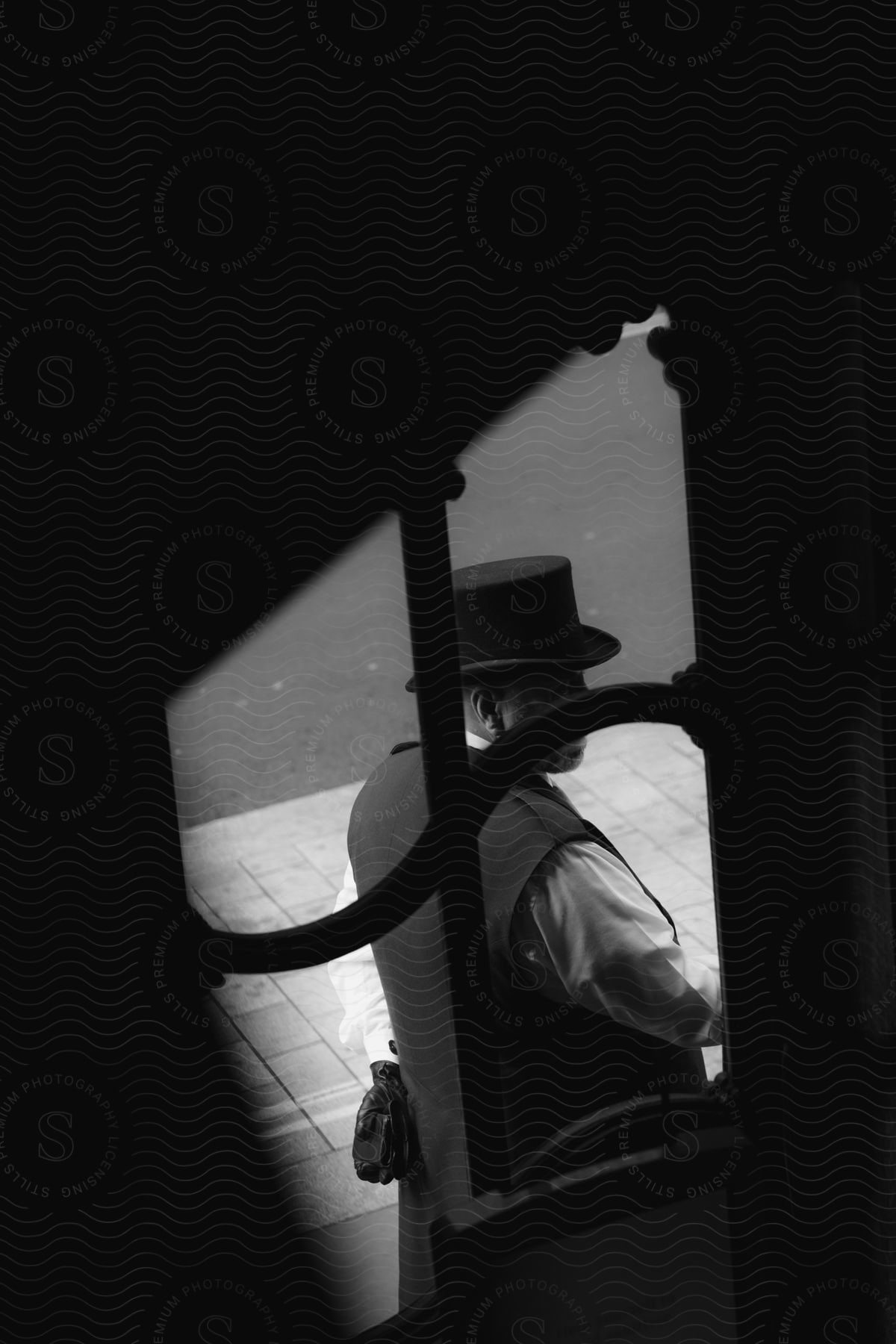 A black and white of a doorman standing outside of a gate on a sidewalk