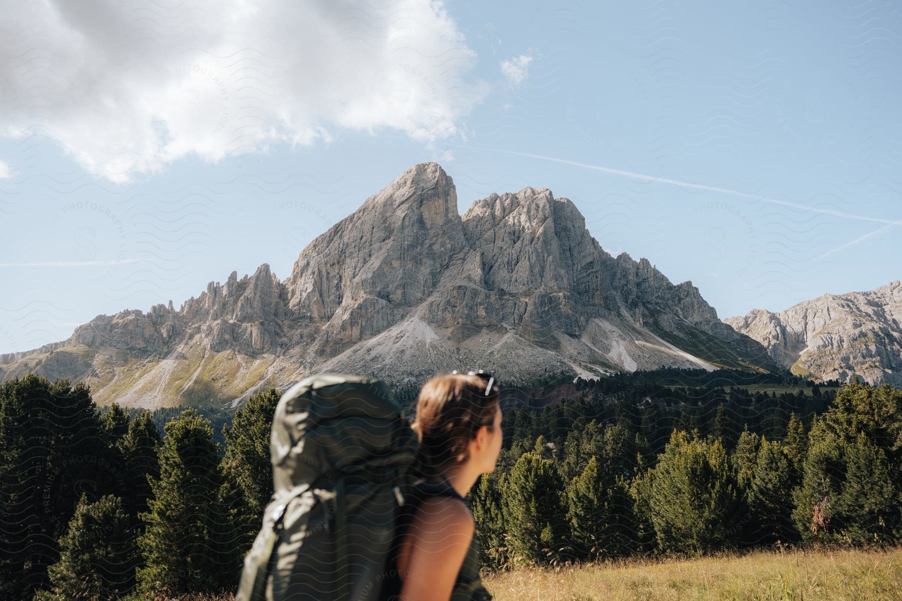 A woman walking outdoors with a backpack on heading toward a mountain