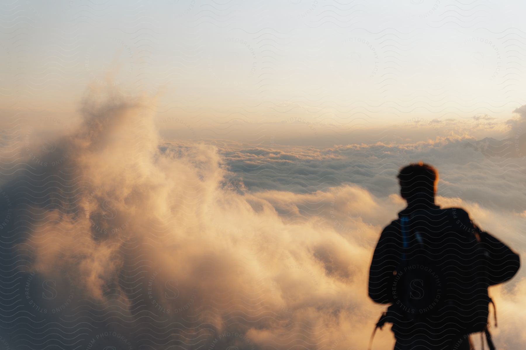 A hiker stands atop a mountain, clouds stretching to the horizon beneath his feet.