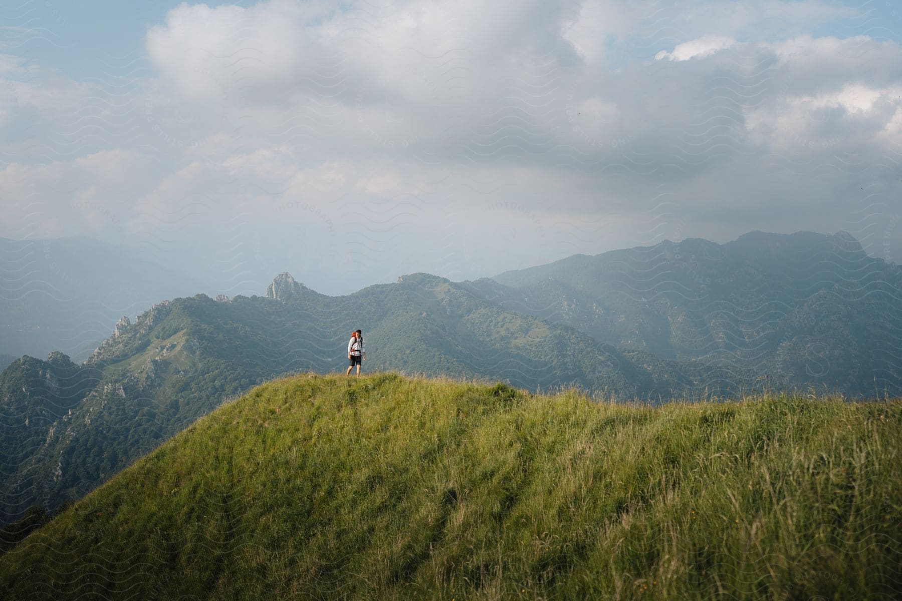 A man is walking on a grassy hill backpacking.