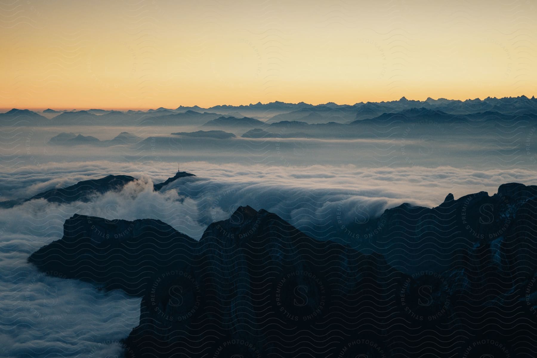A landscape from the top of a mountain of stones where it shows a horizon full of mountains and clouds in a sunset.