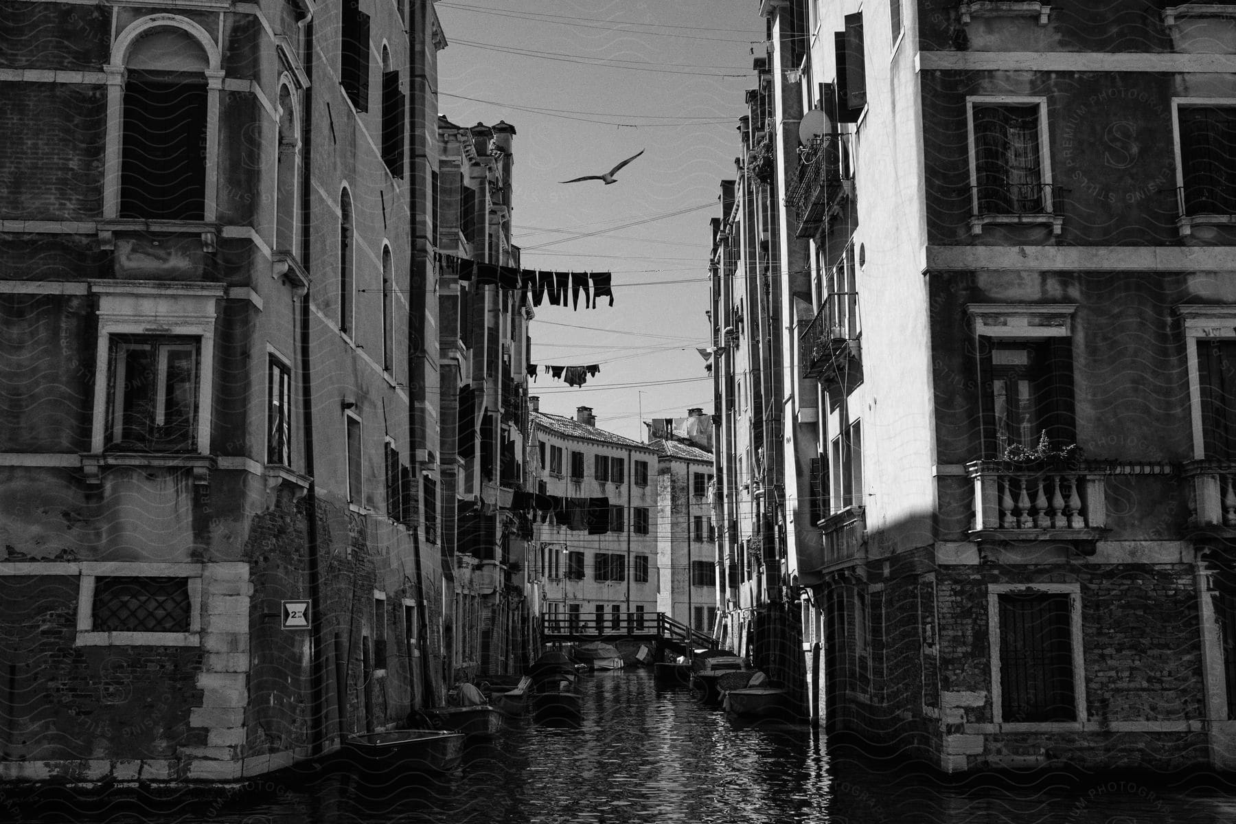 A black and white of city buildings with a river going through them and clothes hanging on lines from windows out of the building.