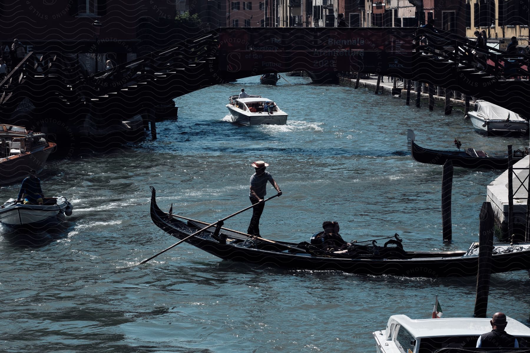 Stock photo of gondolier steering gondola in the river as motor-powered boats go by.