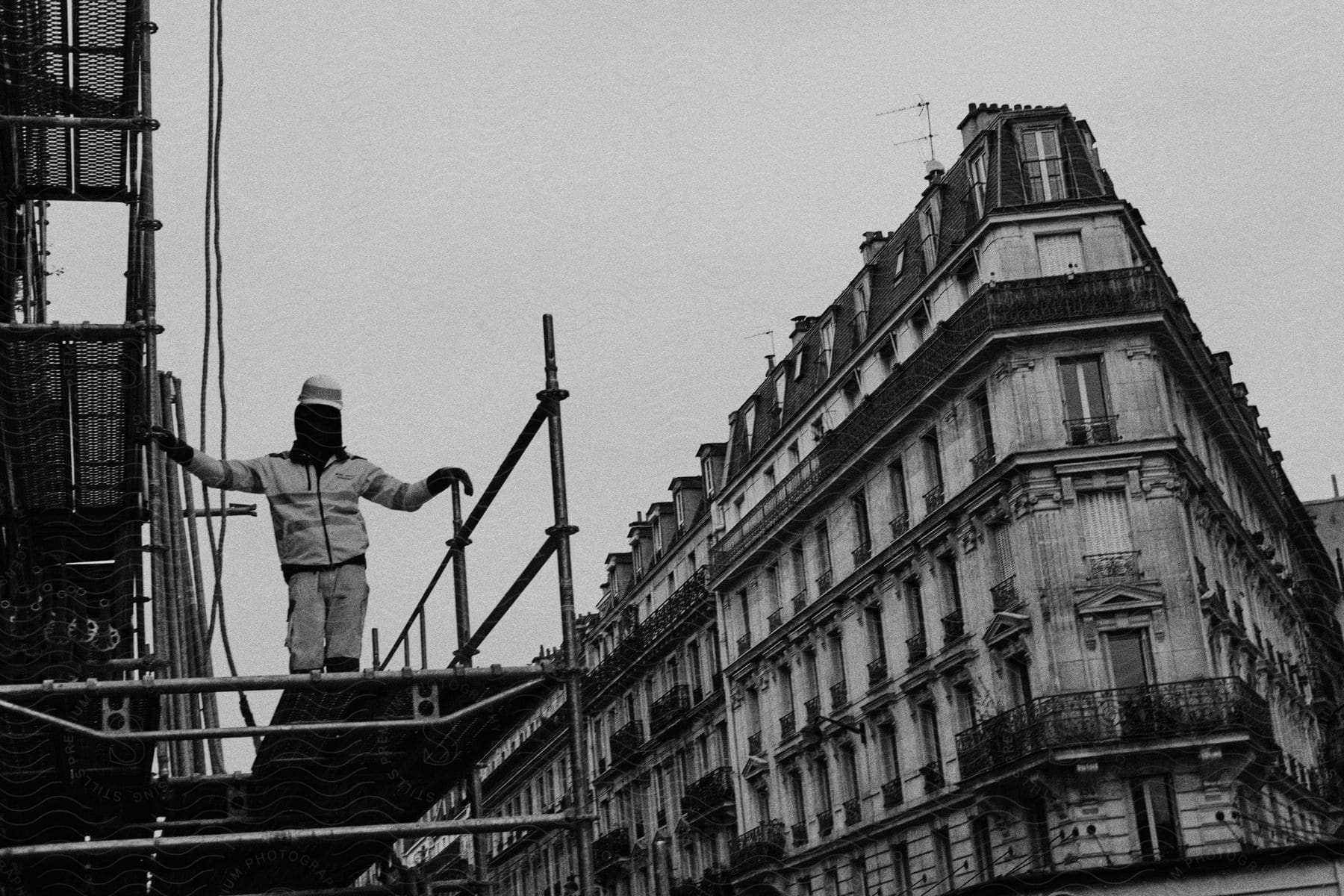 A construction worker poses for a photo in a scaffold, in front of a different building.