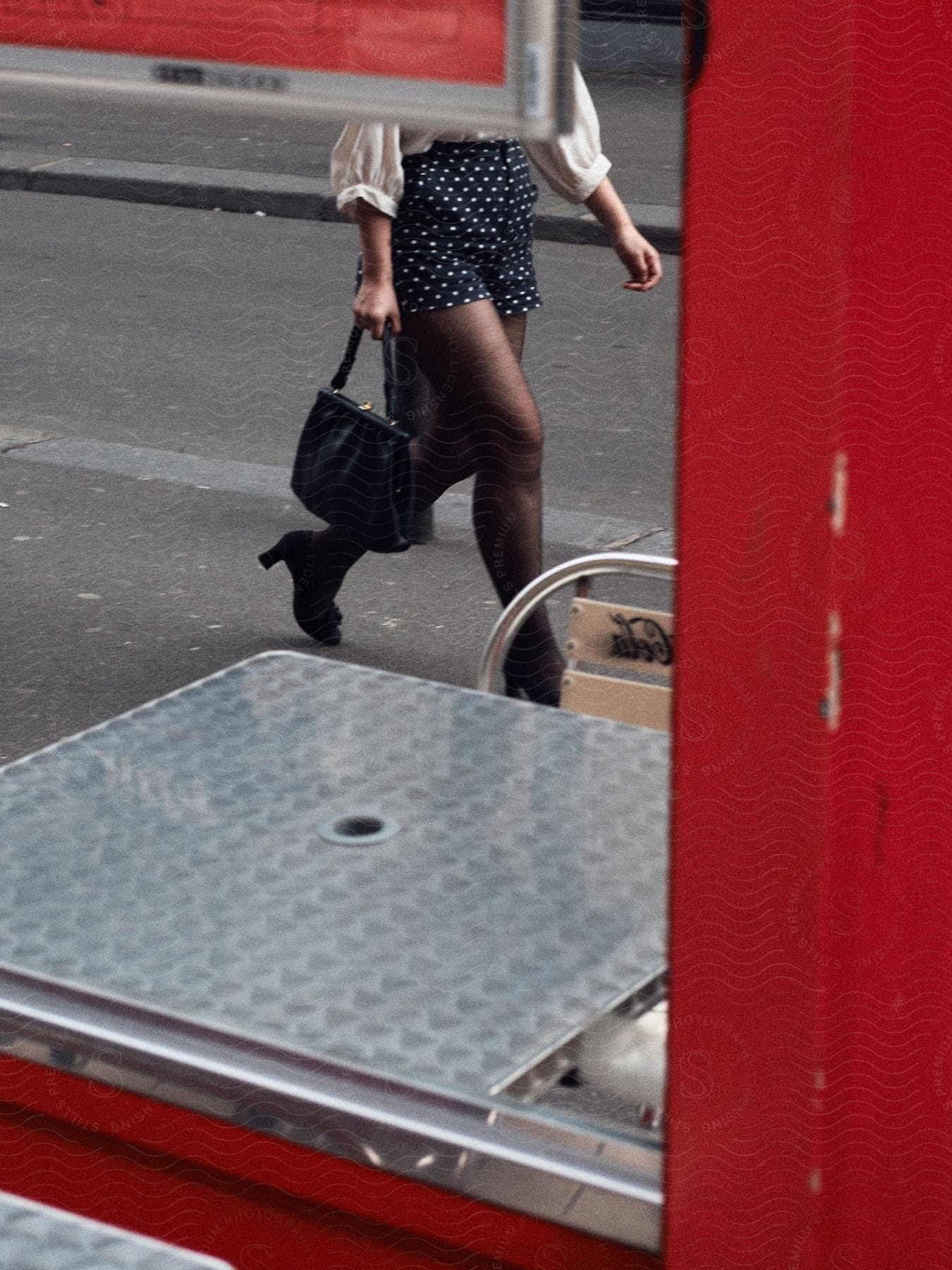 A woman wearing dark polkadot shorts and a white blouse is carrying a black handbag as she walks on a street near a fire truck