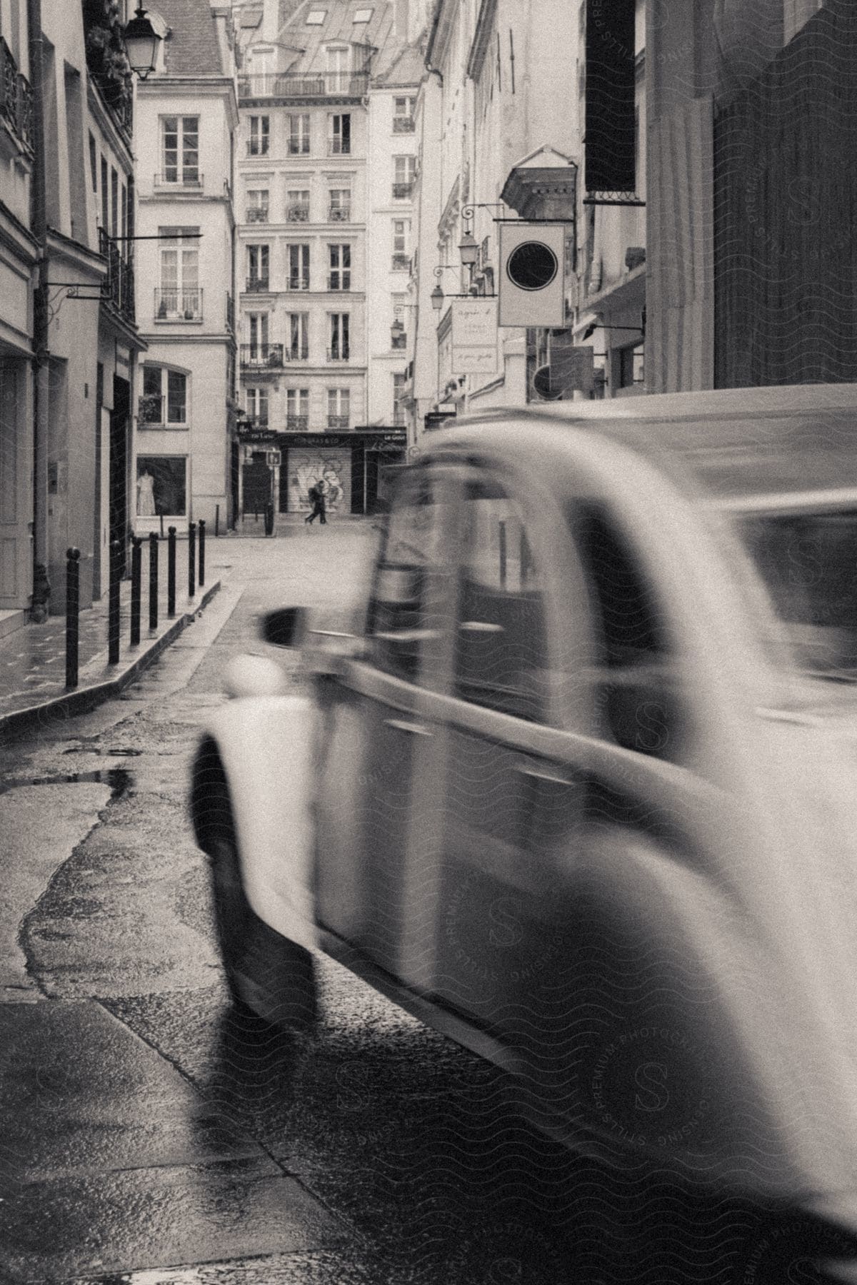 Stock photo of a vintage car drives down narrow european street lined with tall historic residential buildings.