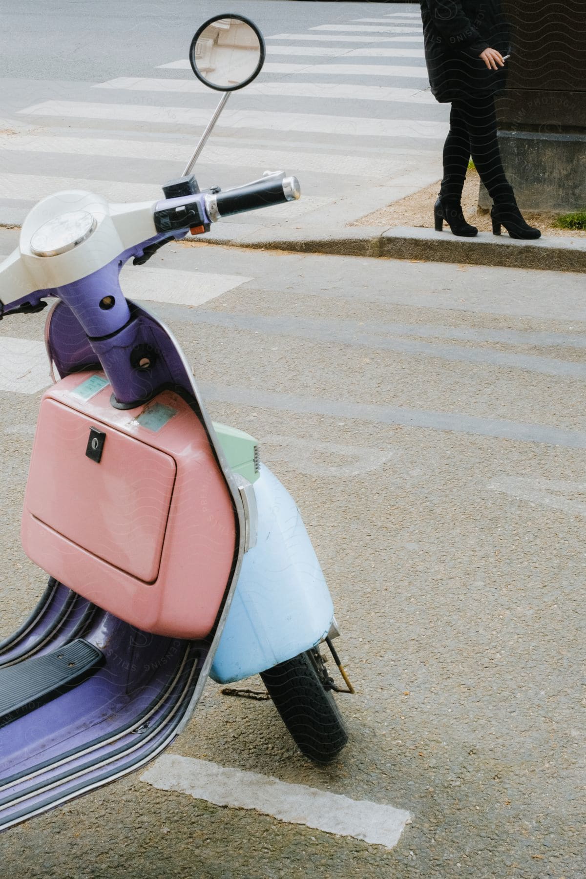 A Vespa is parked on the street as a woman walks near a building