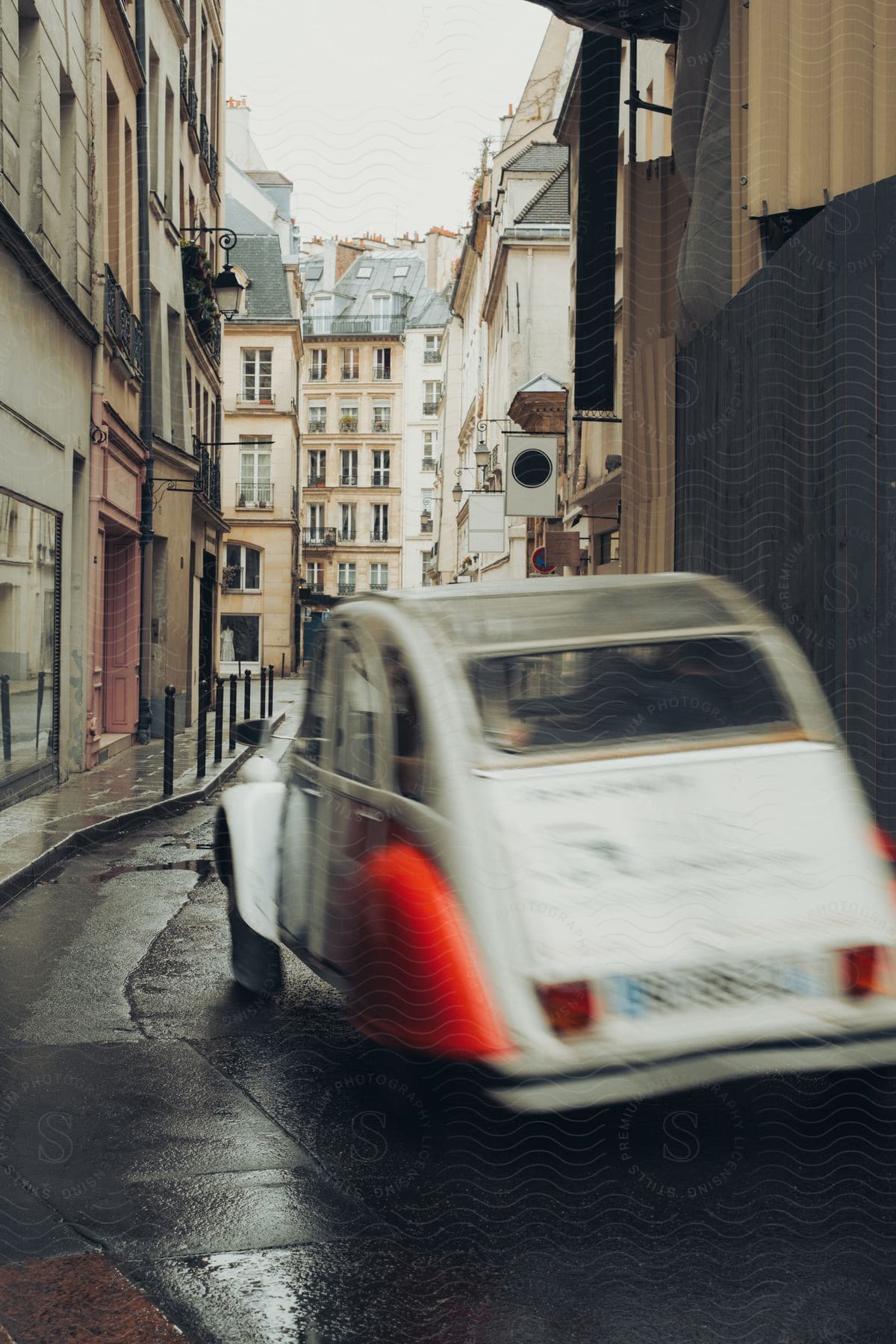 White car with red fenders driving down a rain-soaked street in an urban neighborhood.