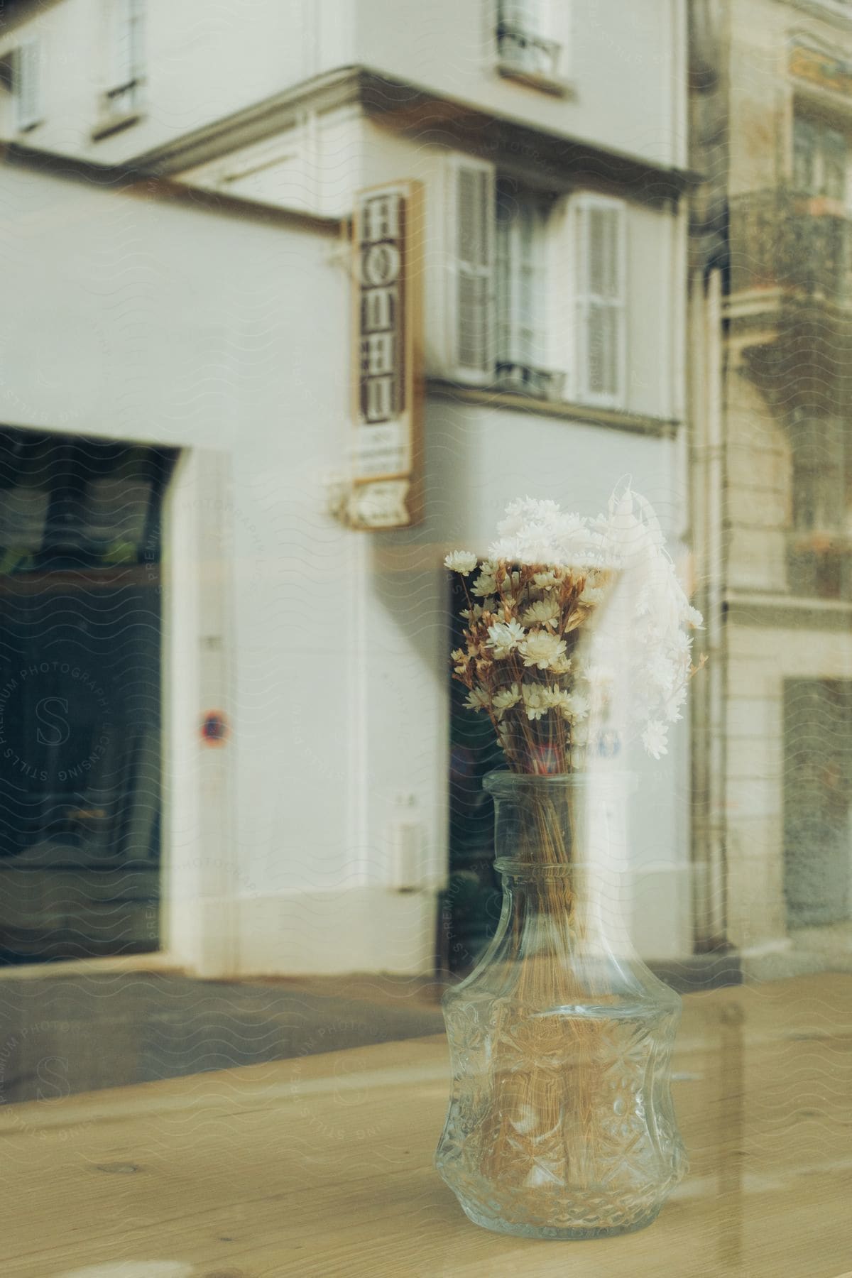 Window looking onto hotel reflects flowers in glass vase.