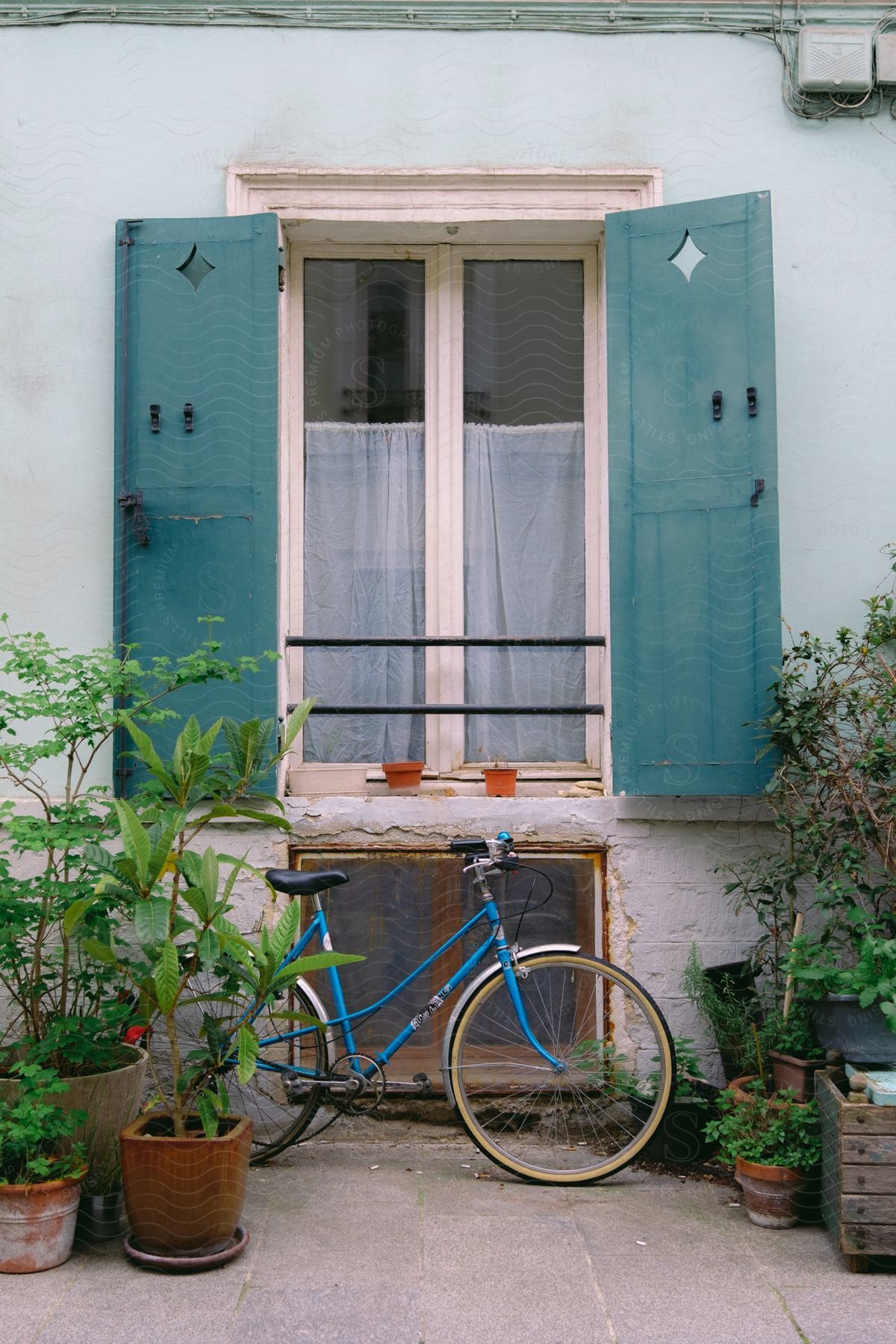 A blue bicycle sits outside below an apartment window with blue shutters.