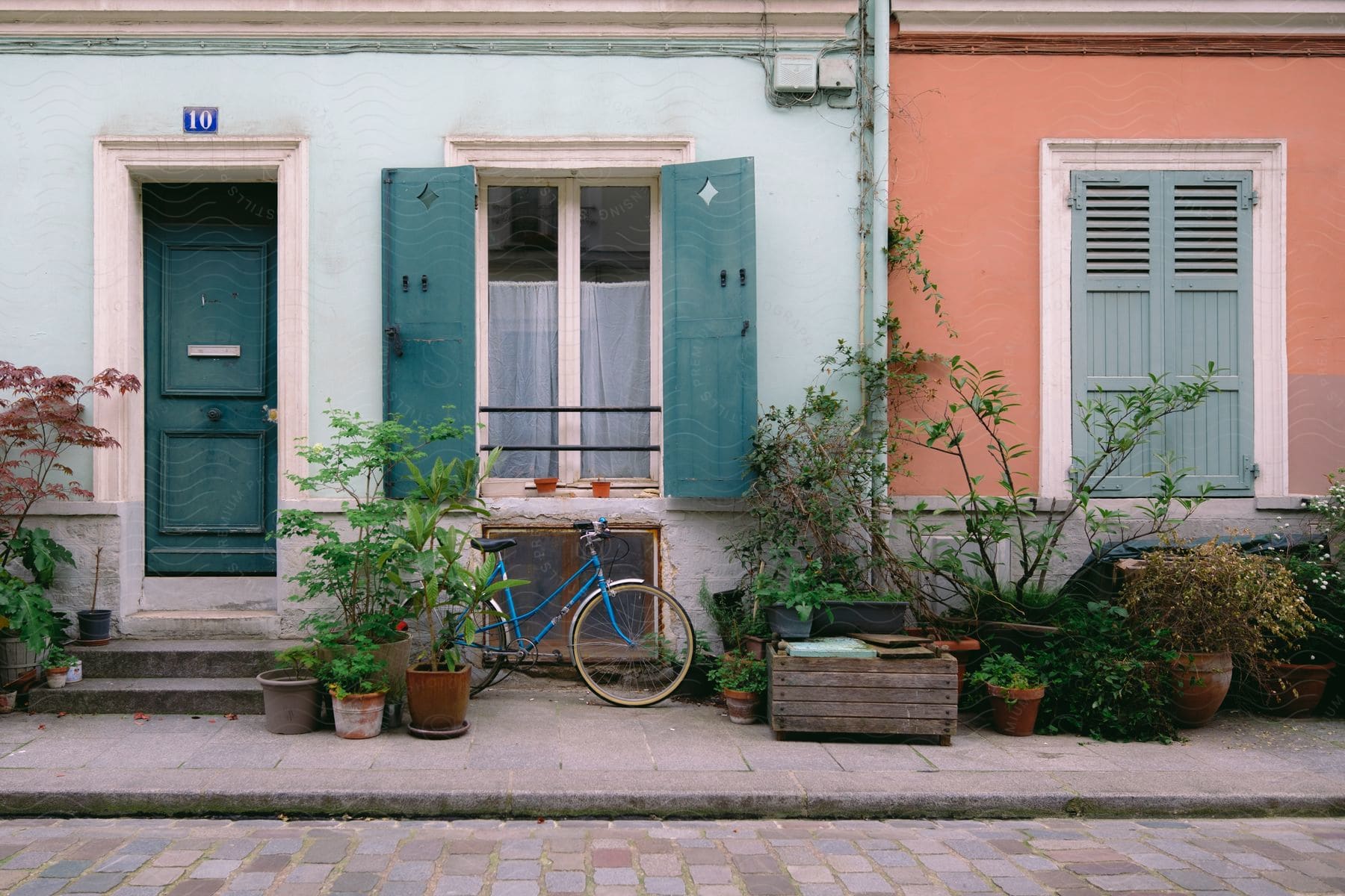 An apartment building is painted in shades of blue and orange with a blue bicycle and potted plants in front.