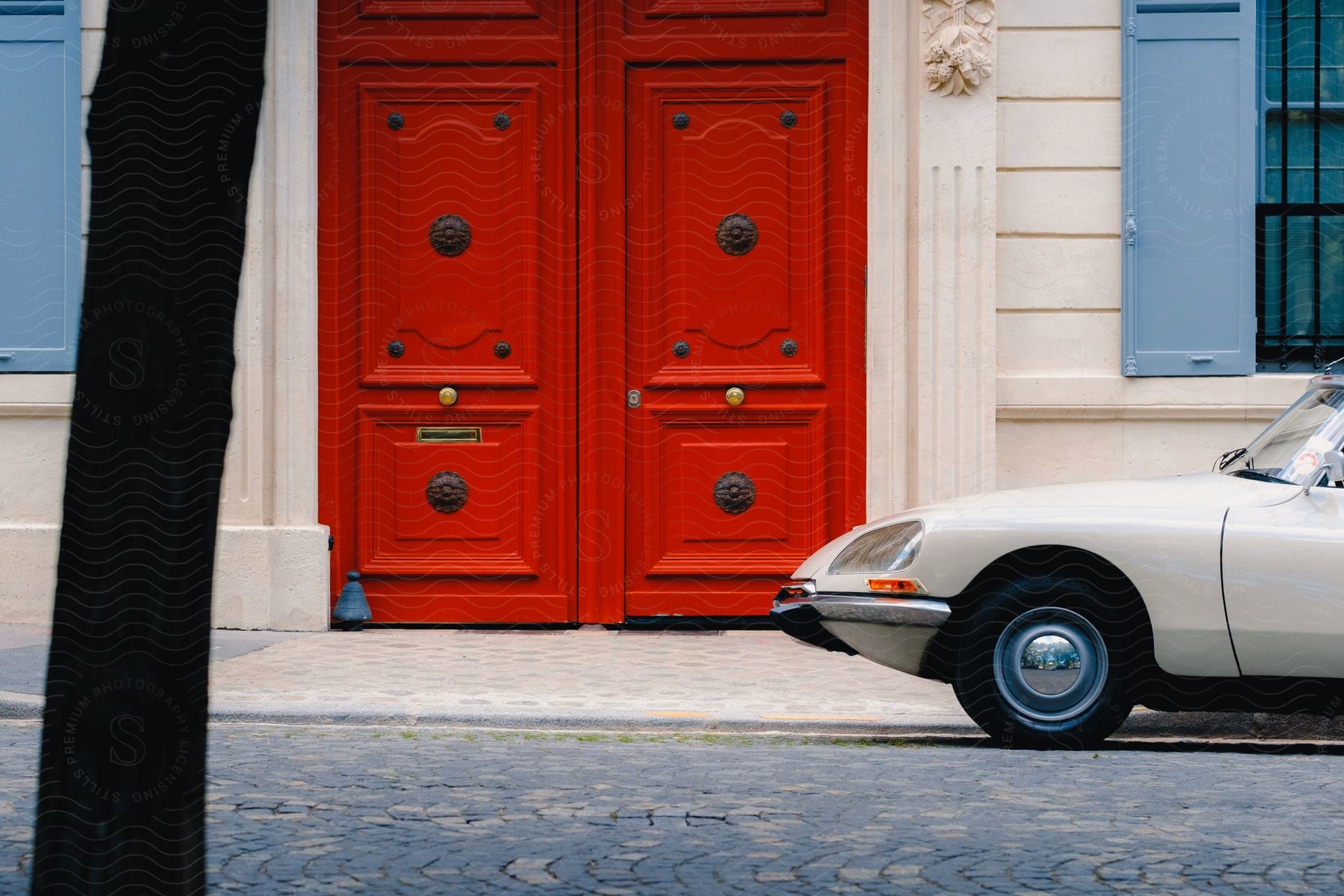 a milk color car parked beside a building with a red door