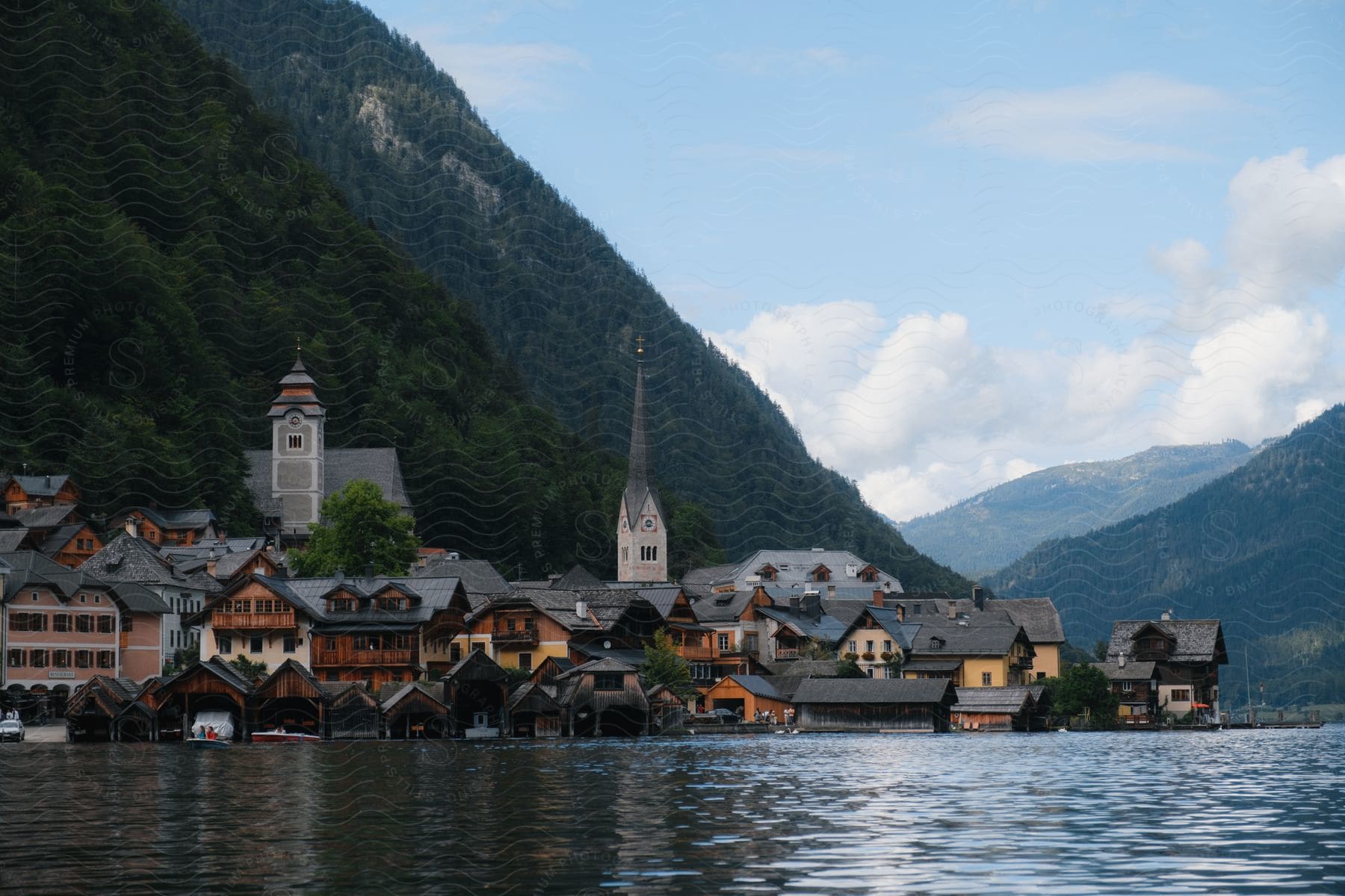 People leave boat house in boat on edge of town nestled against mountain.