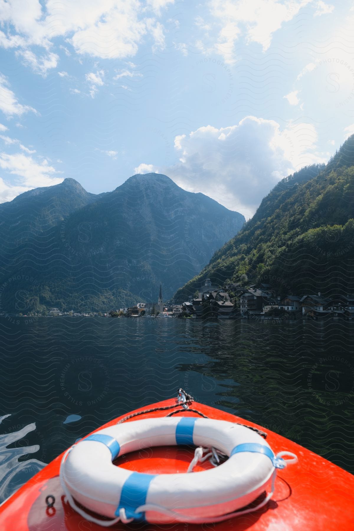 A bright orange boat with a life preserver sailing toward a small coastal town in the mountains.