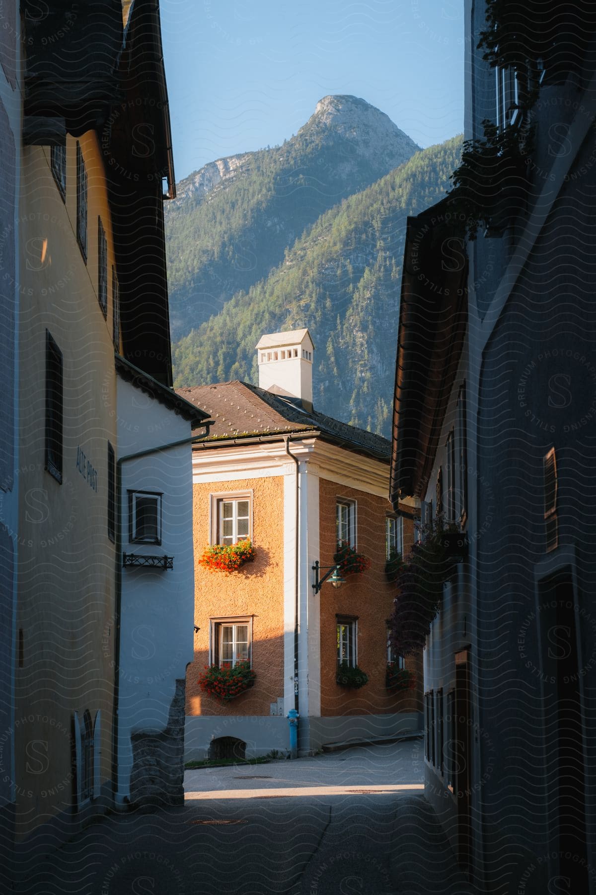 A quaint village with a two-story orange brick building sits below a tall, forested mountain range.