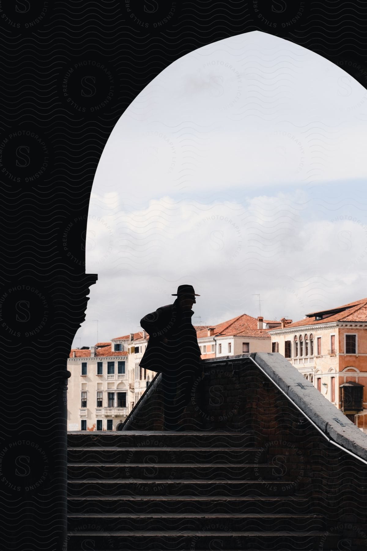 The silhouette of a man in profile and an arch on a bridge overlooking row houses and buildings
