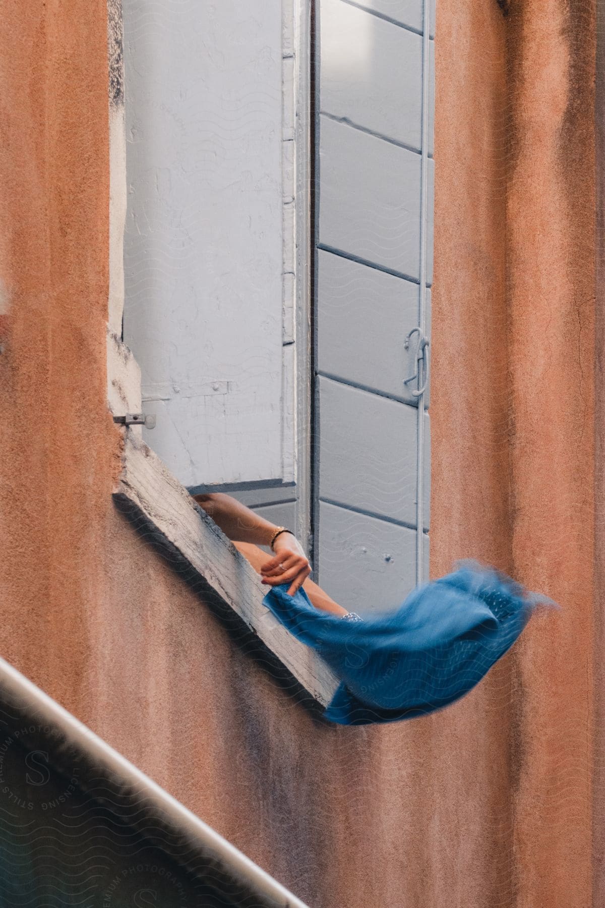 A person's hand is seen outside an apartment building window, carefully spreading a blue cloth on the window