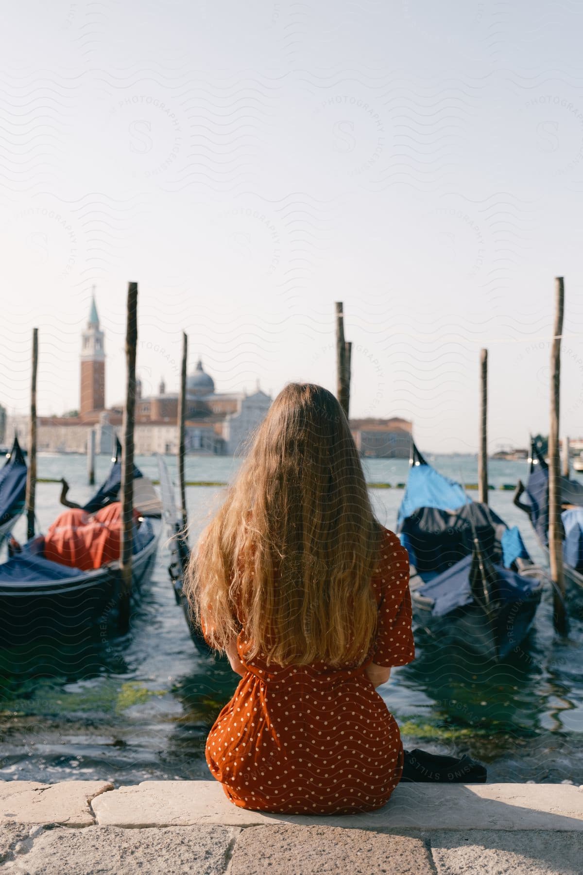 A women is sitting on a dock looking at the city in front of her.