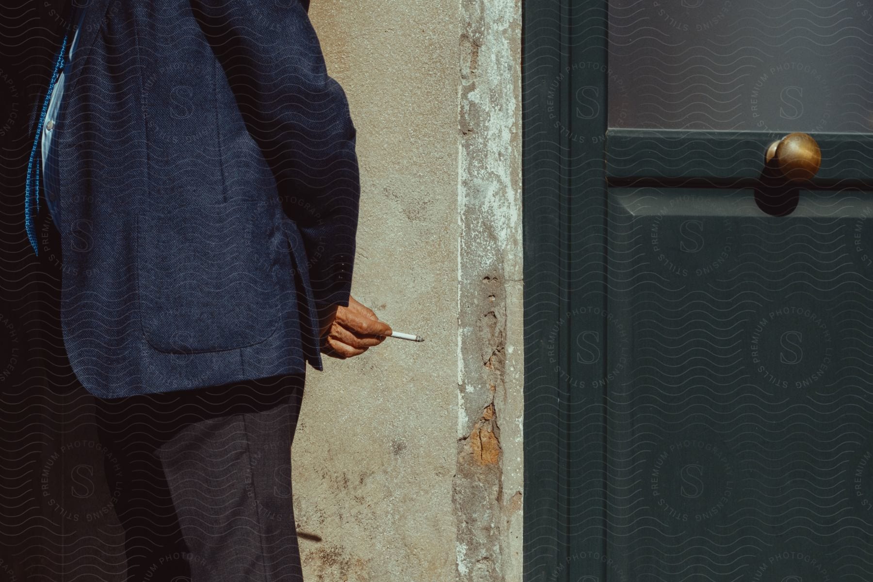 Person wearing suit jacket holding cigarette near a door.