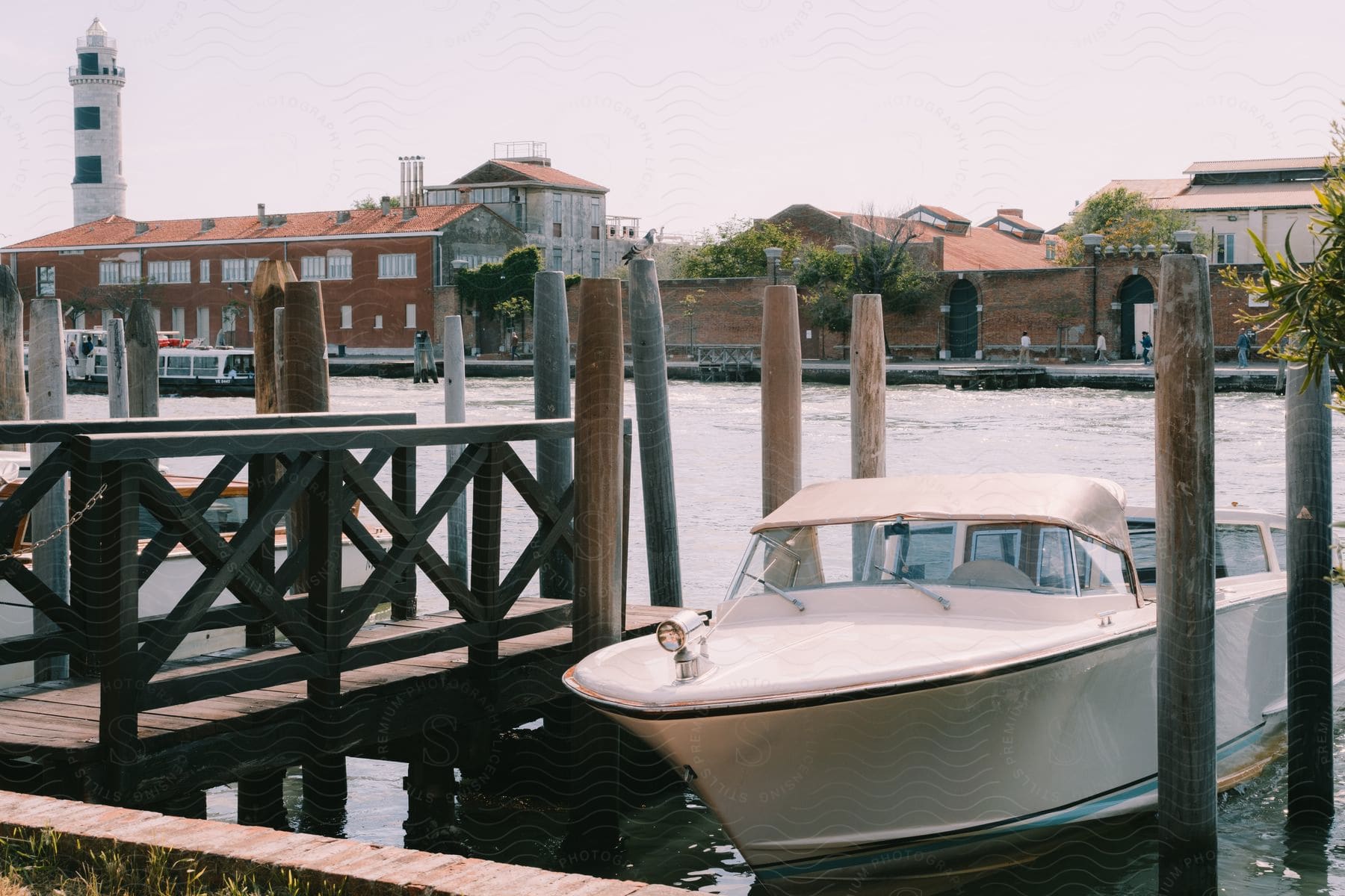 A boat docked in a slip at a wooden pier with lighthouse and buildings on the opposite shore