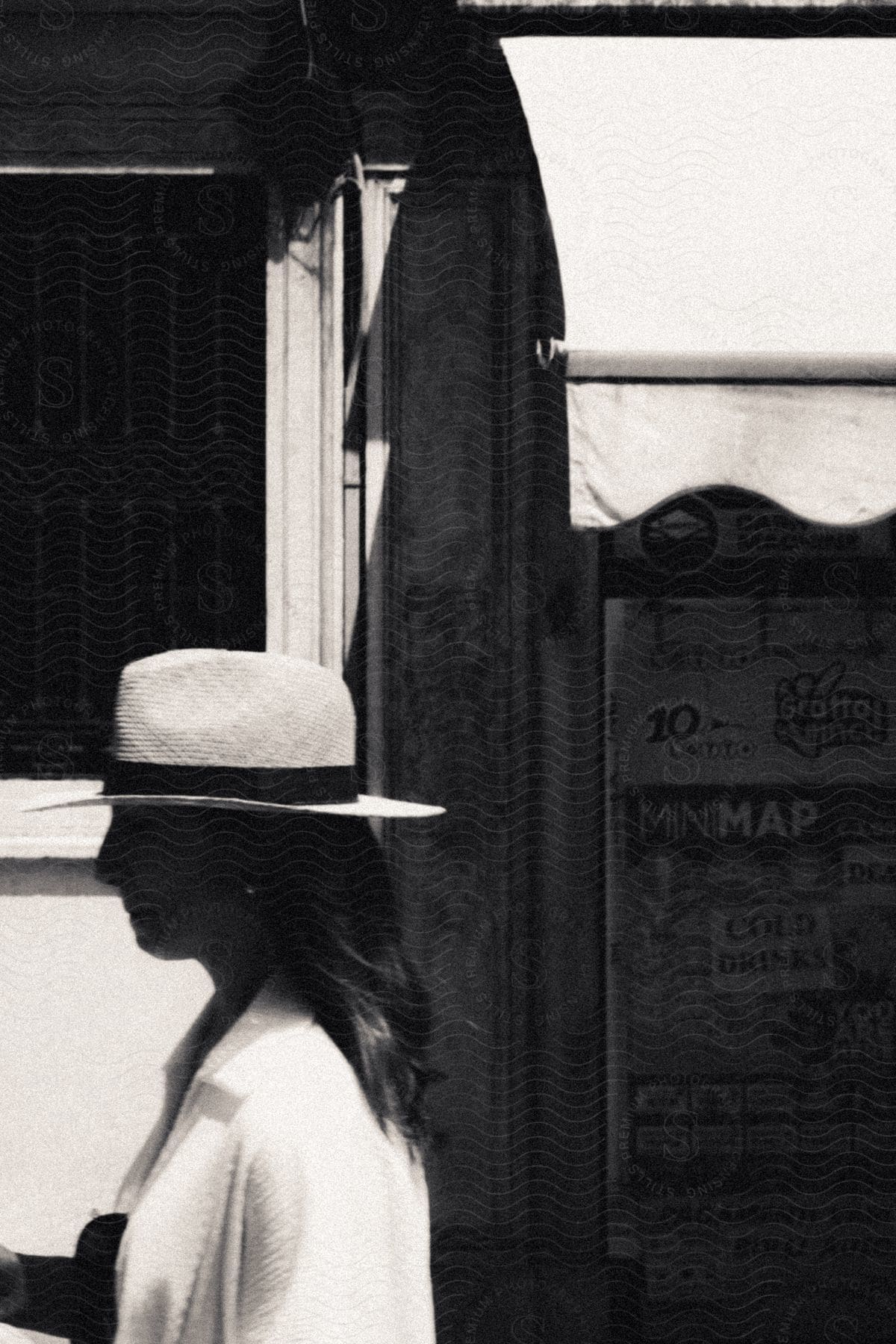 Woman wearing sun hat walks past shop with an awning.