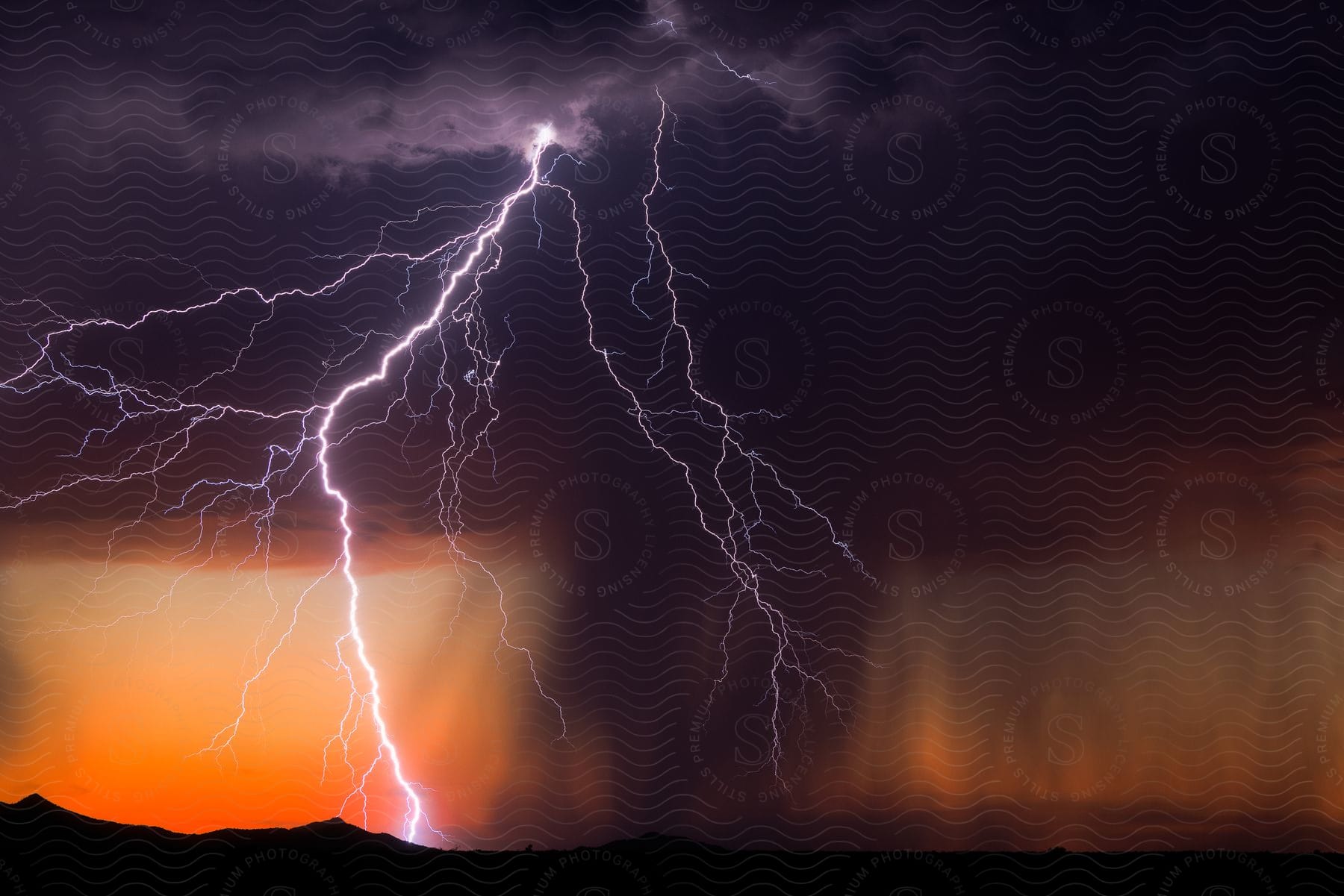 Lightning strikes the sloping hills and plains below amidst a darkened sky at sunset.