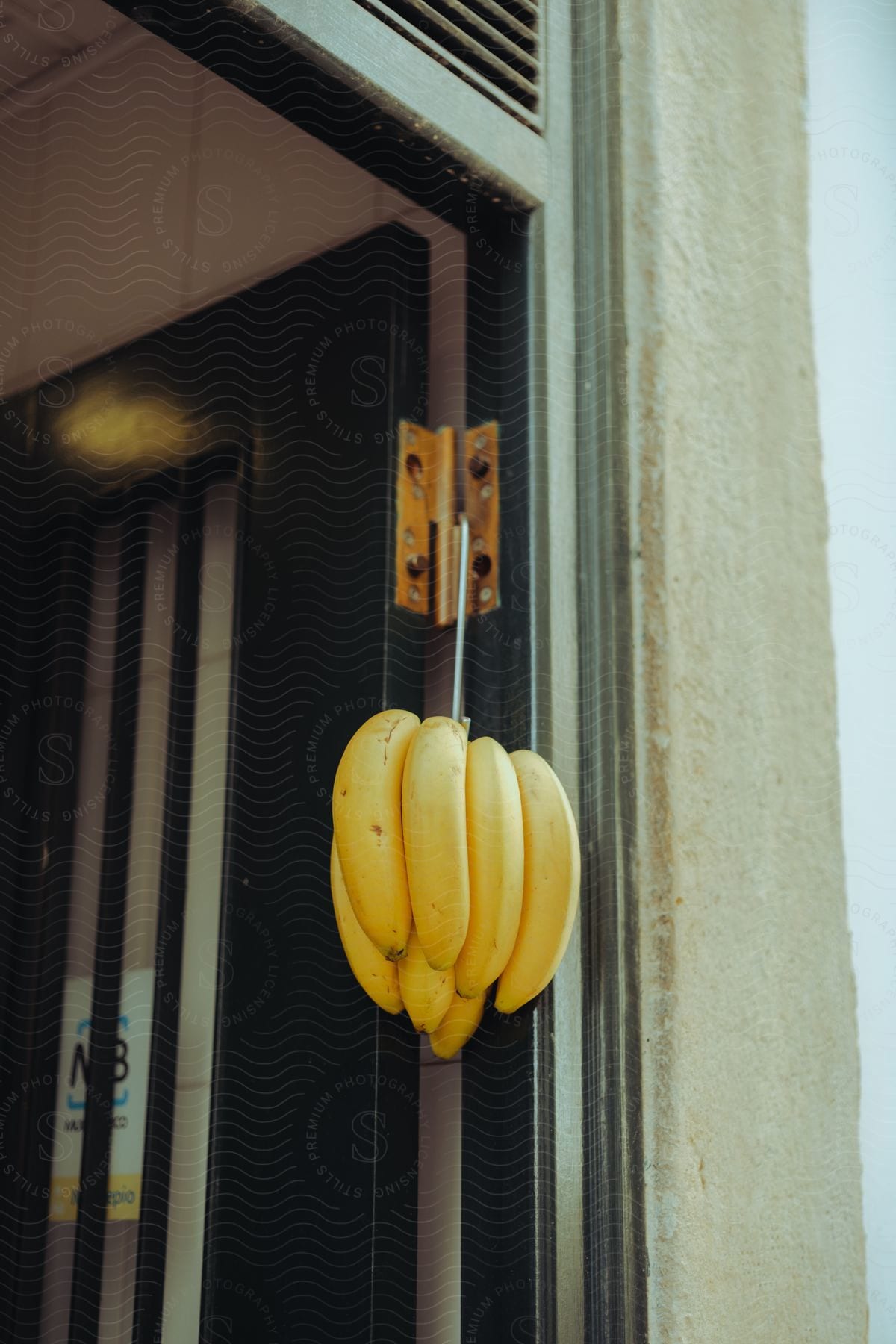 Bunch of yellow bananas hangs on door hinge of open door.