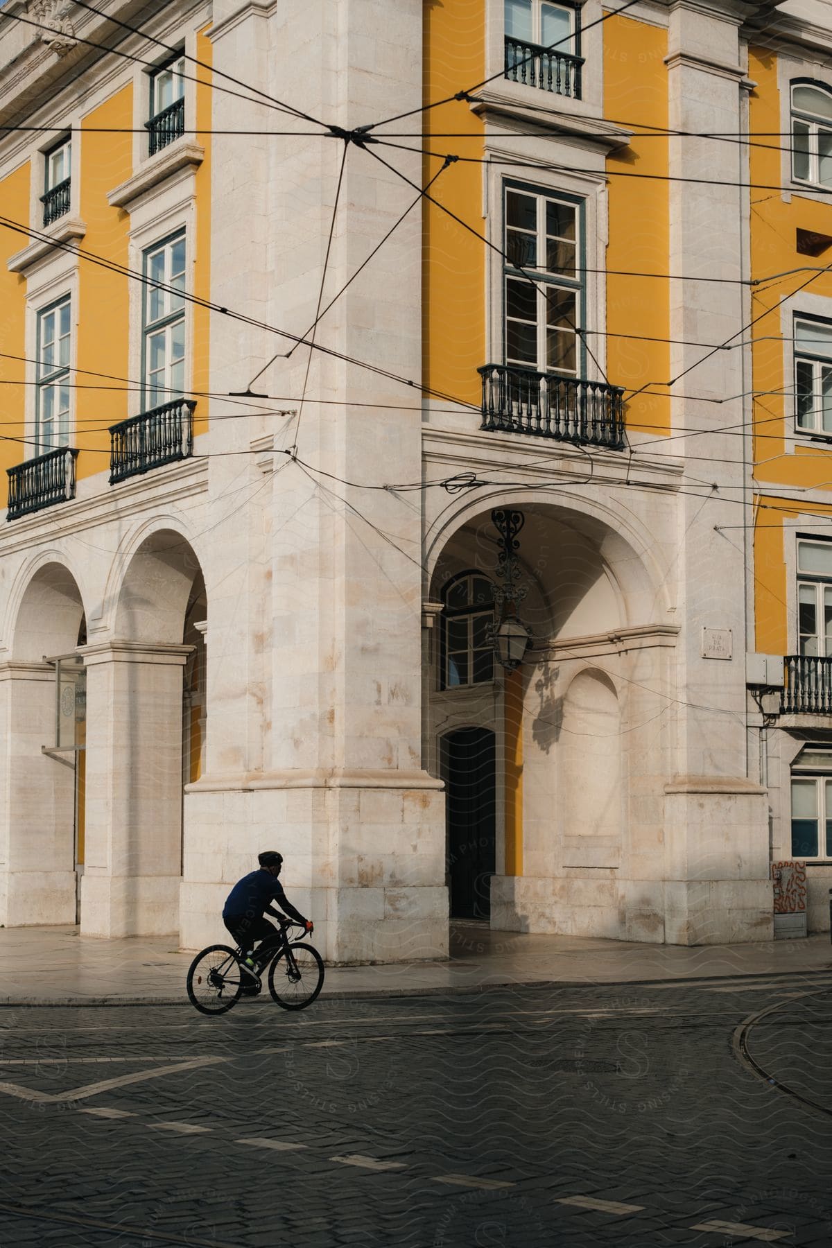 A man cycles past a residential building on a lonely street with series of wires across the street