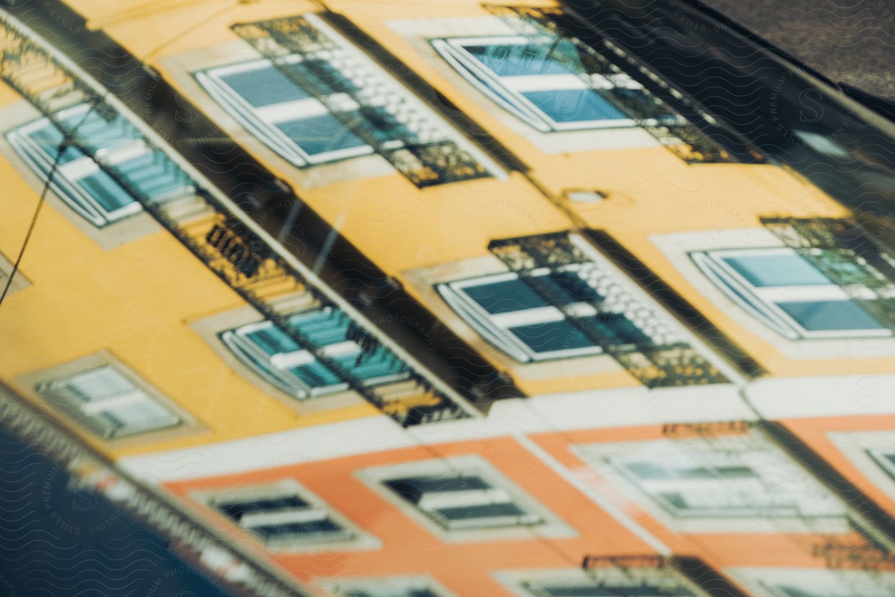 Orange and yellow buildings reflected in the windshield of a car.