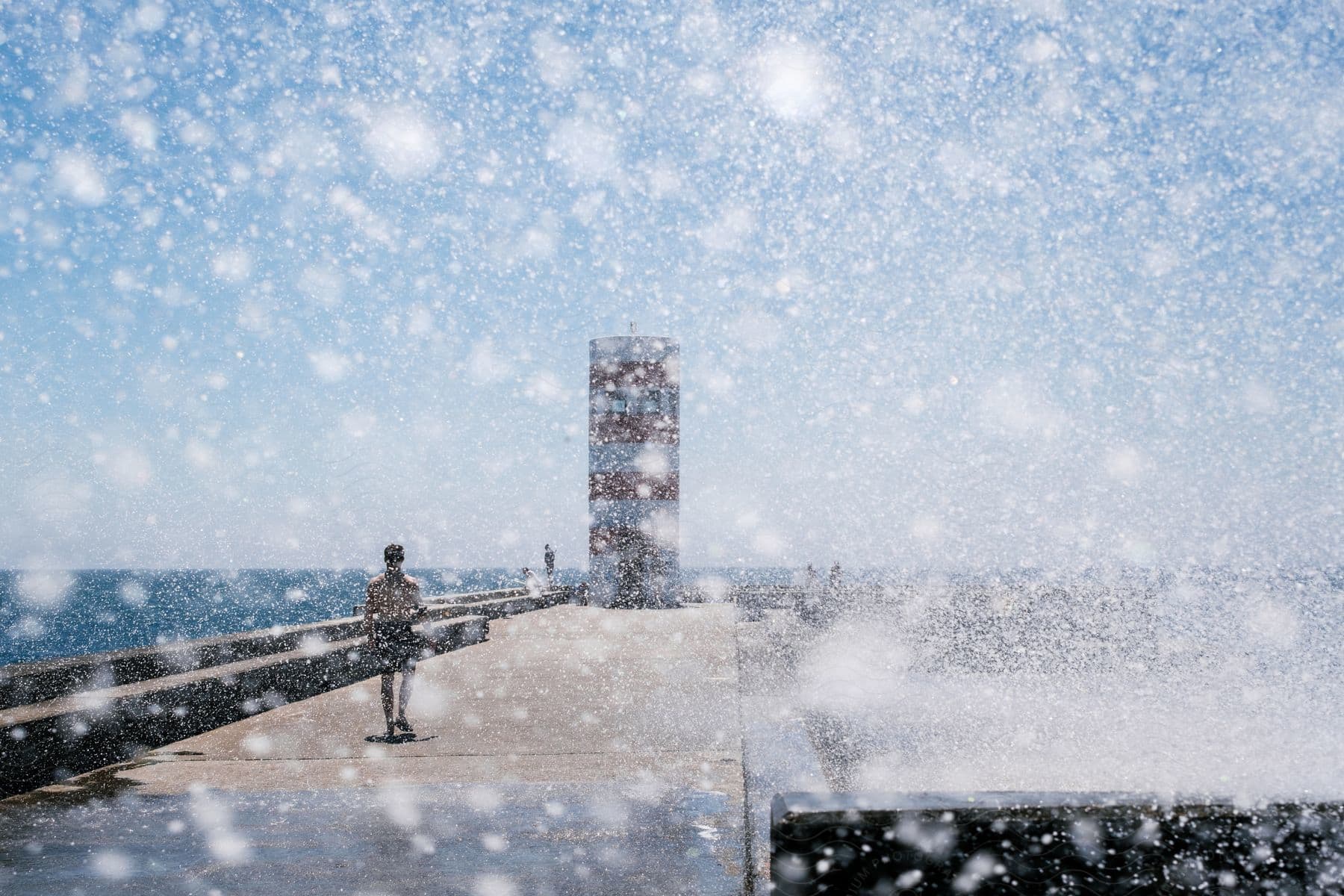 A man walking down a pier seen through a lens covered in sea spray.