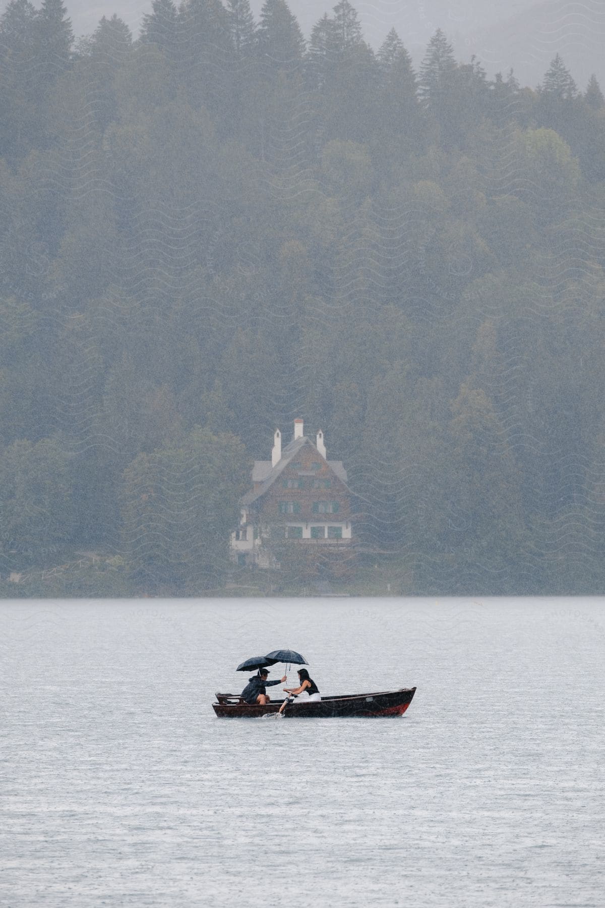 Two people with umbrellas in a rowboat on a lake.