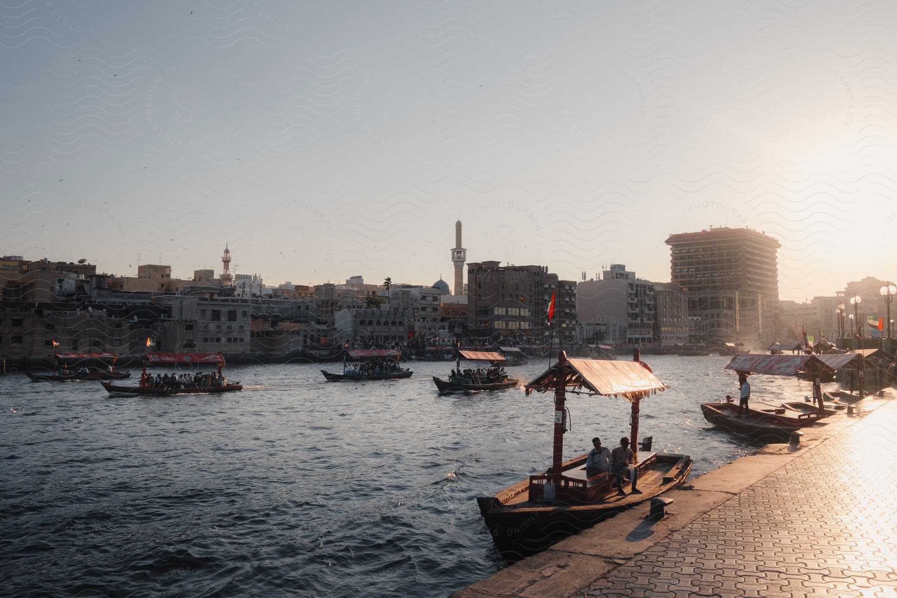 Stock photo of abra boats filled with people sail in the water off the coast of a city in dubai