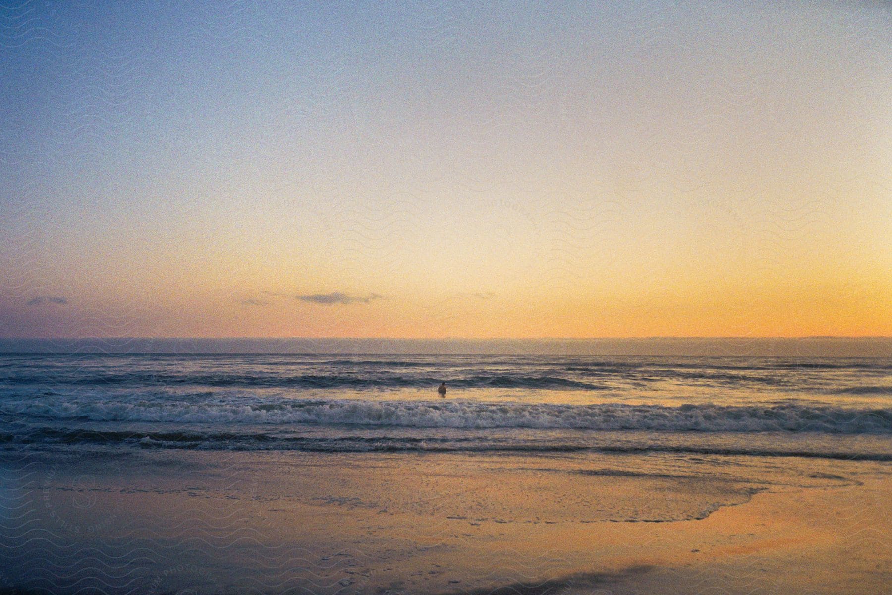 a person standing in the ocean as waves come ashore at sunset.